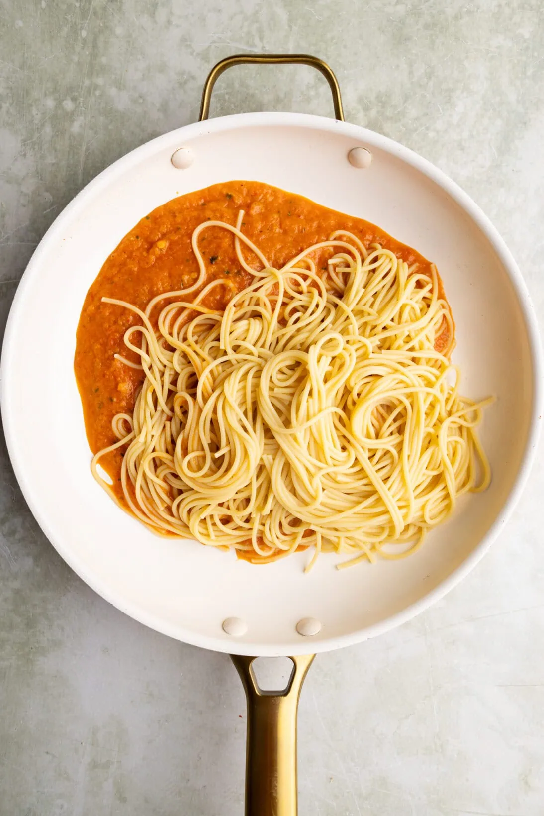adding pasta to a pan with the roasted red pepper sauce.