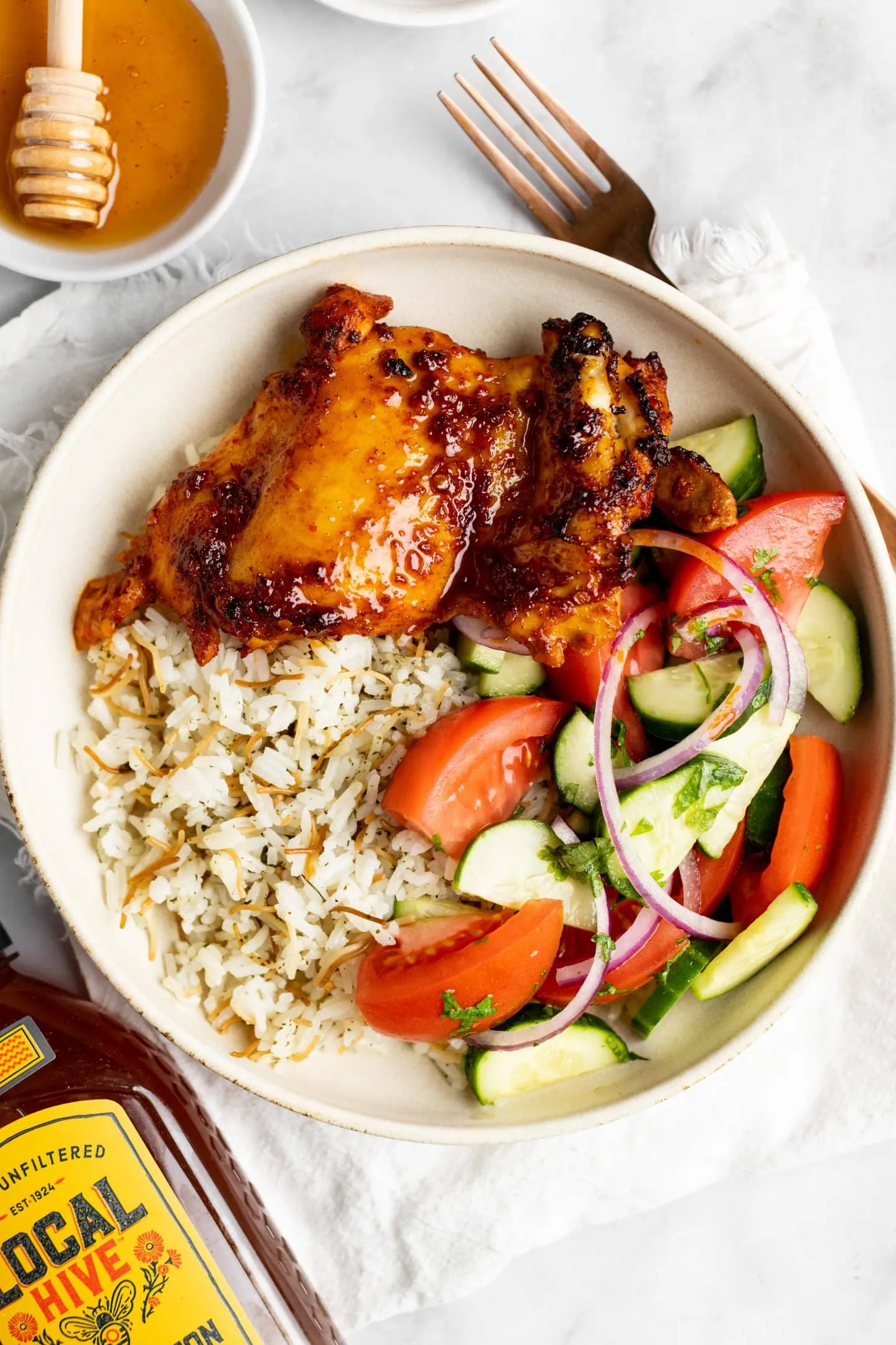 up close bowl of harissa honey chicken with rice and side salad.
