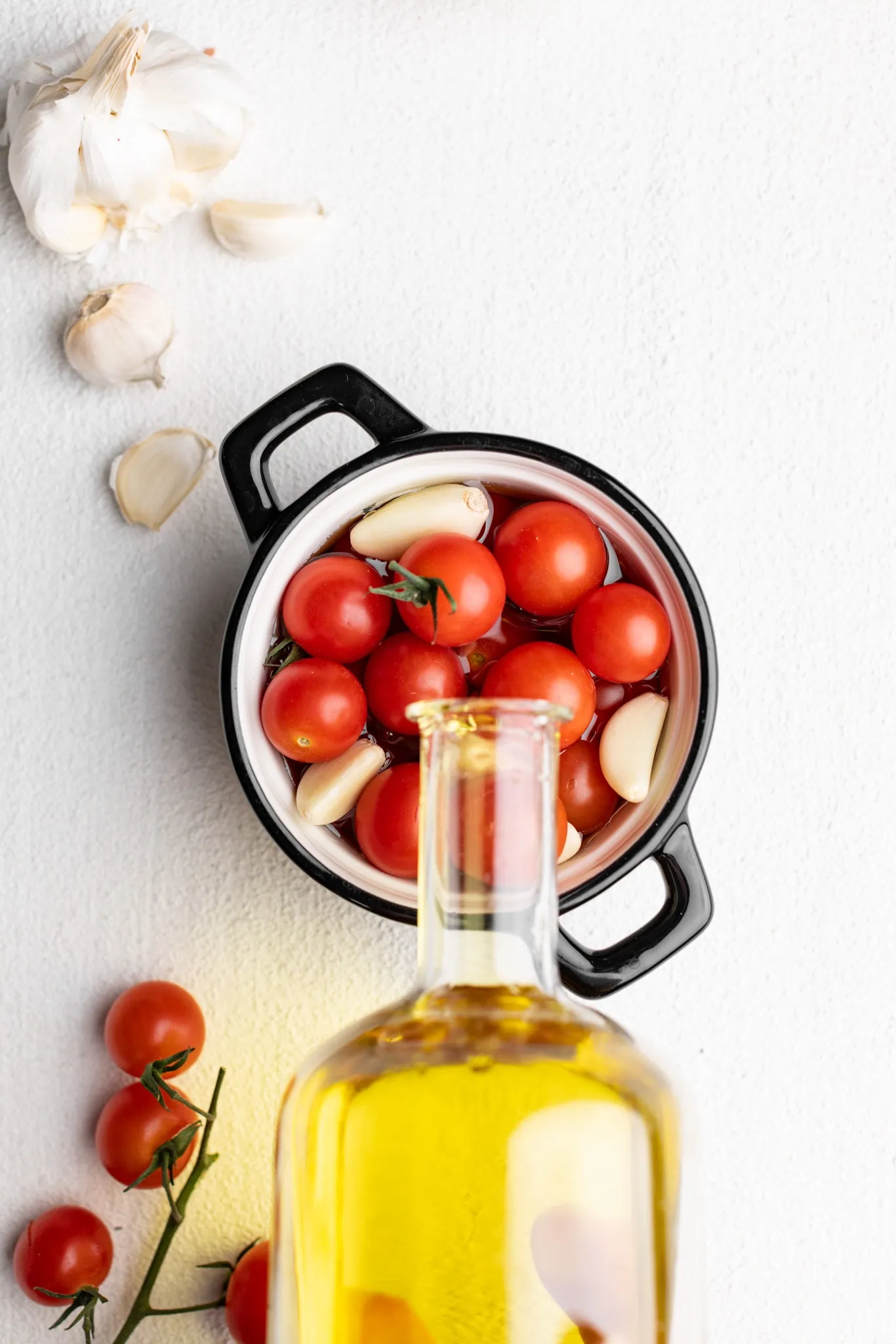 pouring oil in a croquette with cherry tomatoes and garlic.