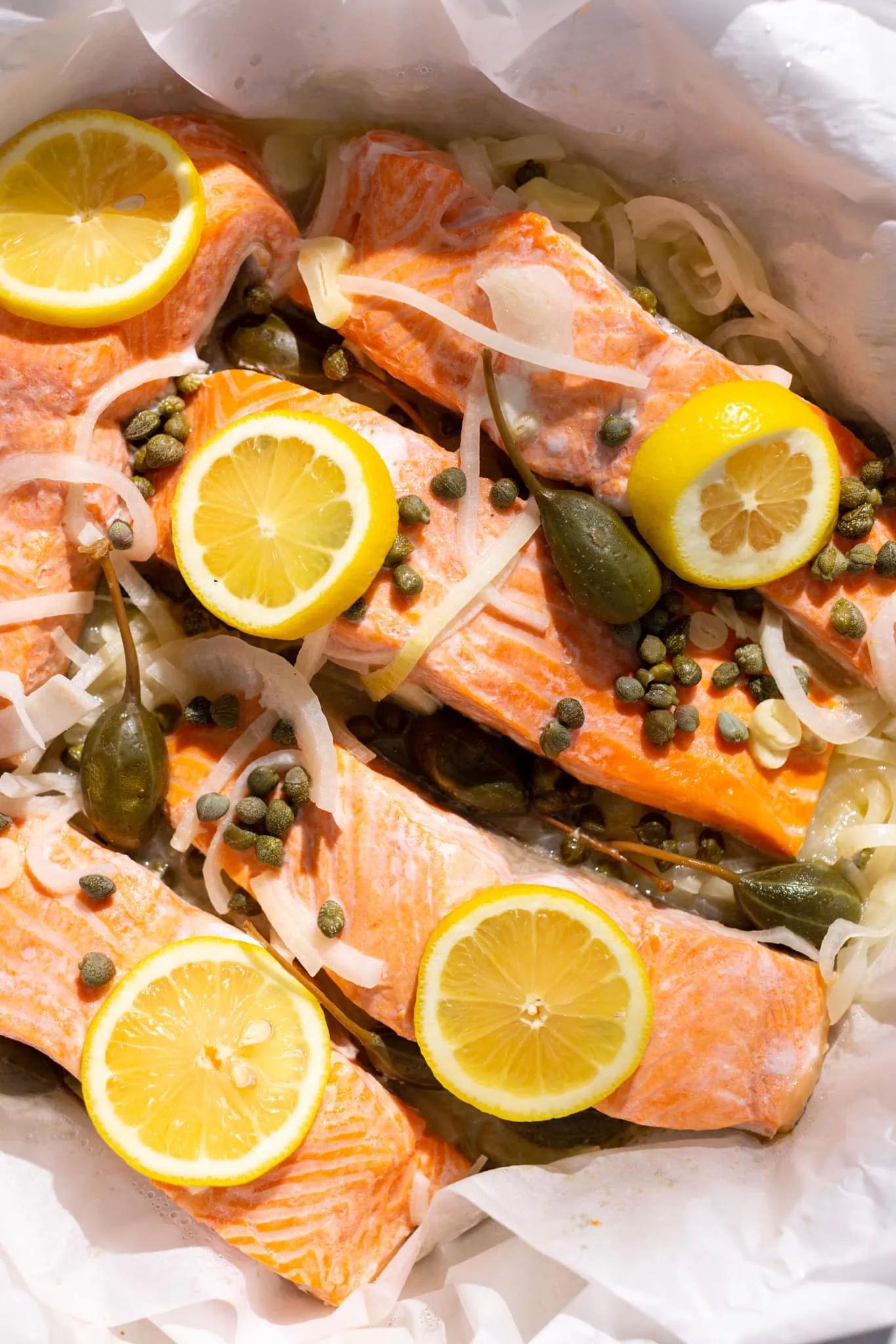 cooked steamed salmon with onions, garlic, capers, and lemon slices.
