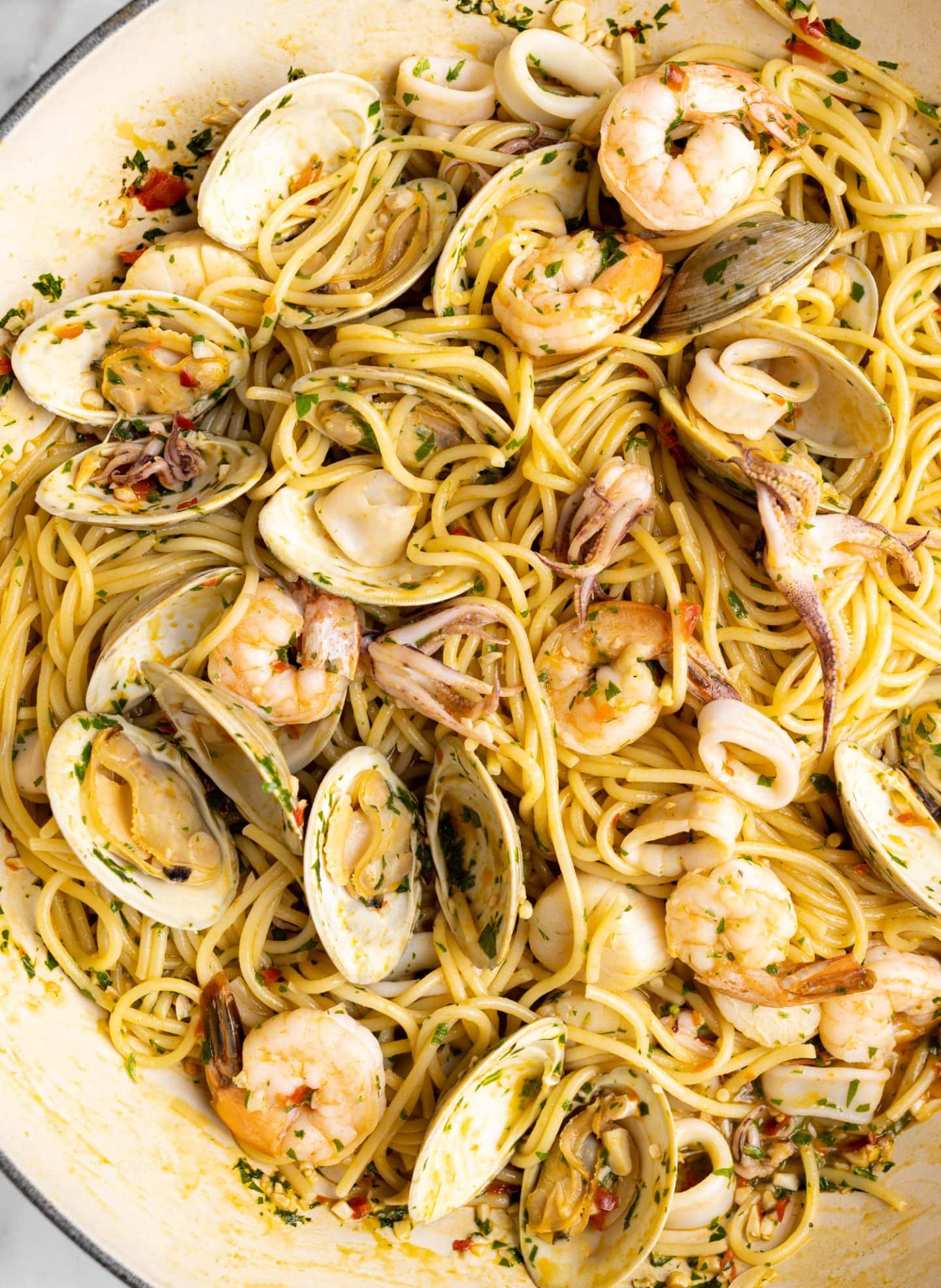 up close shot of seafood pasta in a braiser. (clams, squid, squid, and shrimp, over linguini)