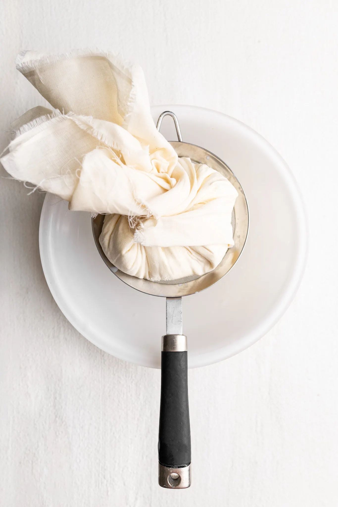 greek yogurt in a cheese cloth over a strainer, cheese cloth twisted.