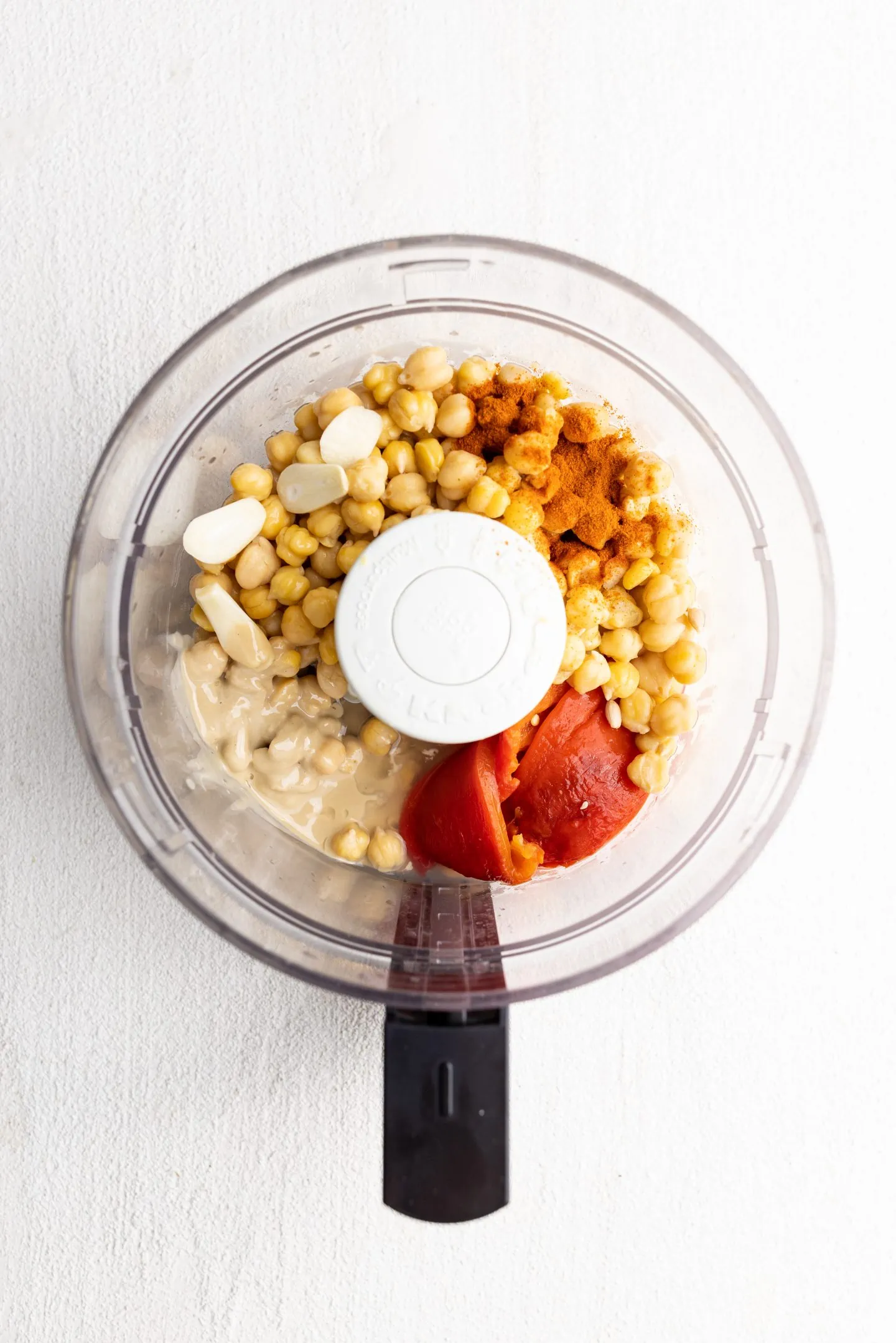 food processor with chickpeas, garlic, tahini, roasted red peppers, and paprika.