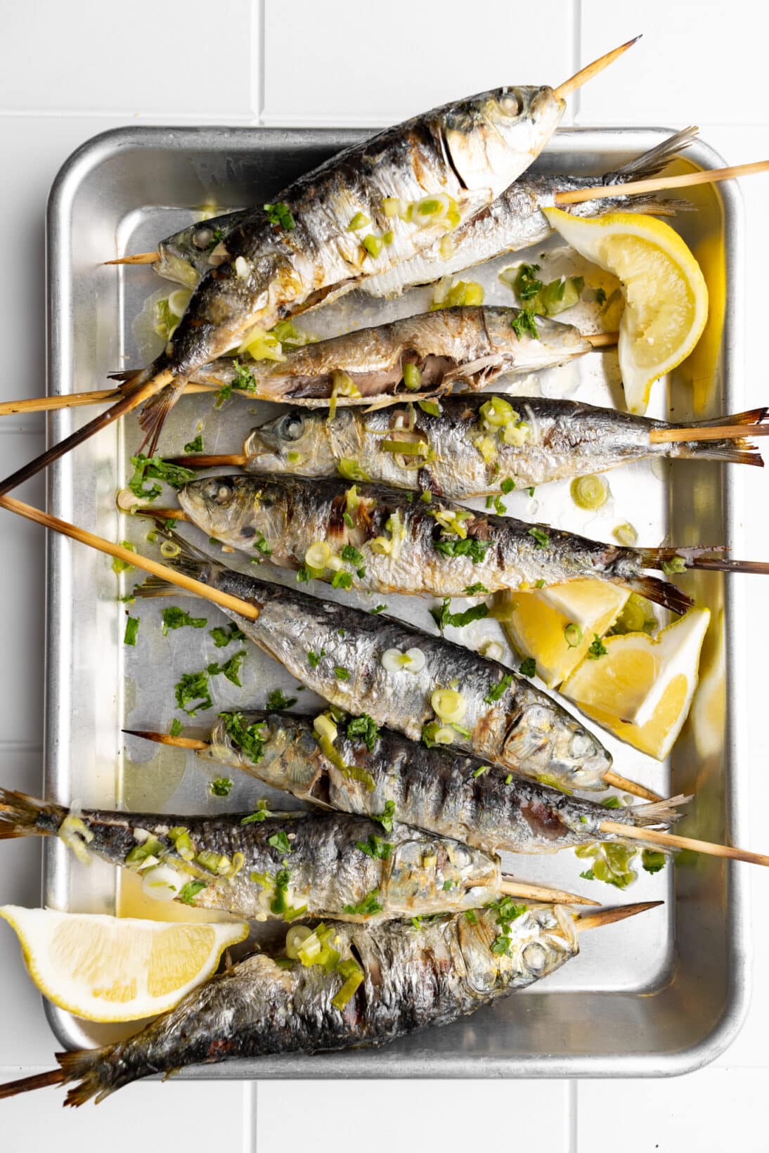 grilled Portuguese sardines on a tray topped with a spicy green onion sauce