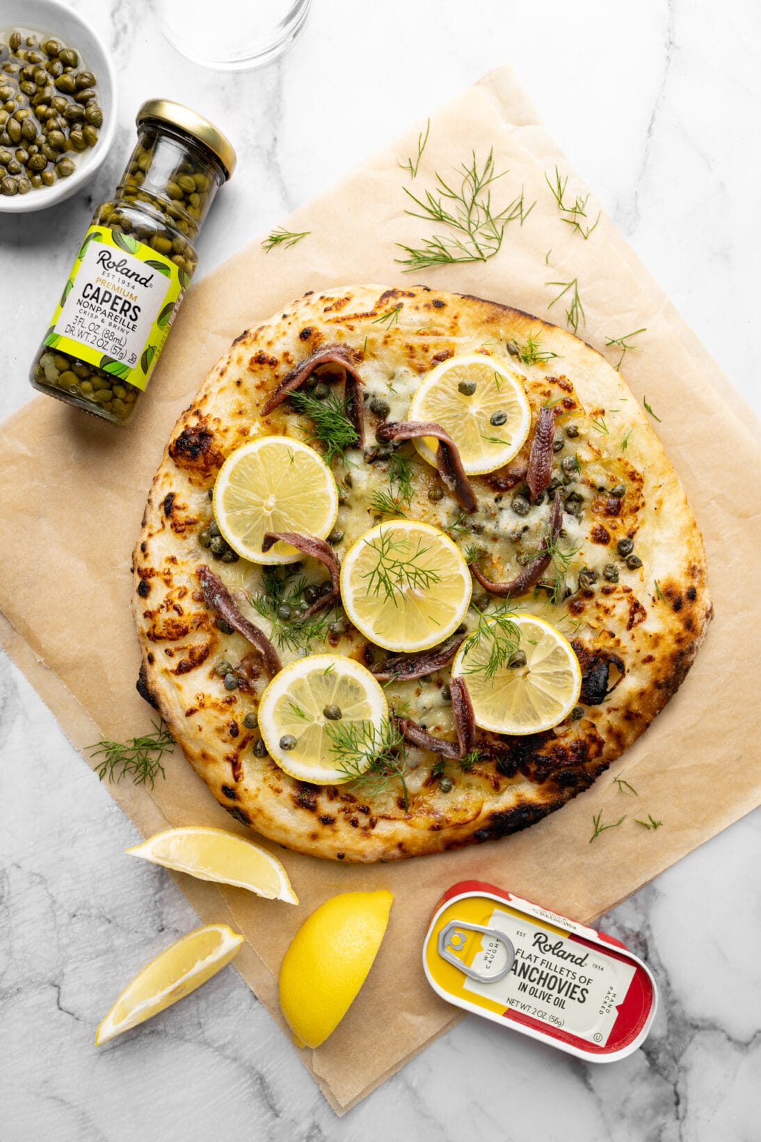 lemon anchovy pizza next to a tin of roland anchovies and a jar of roland capers