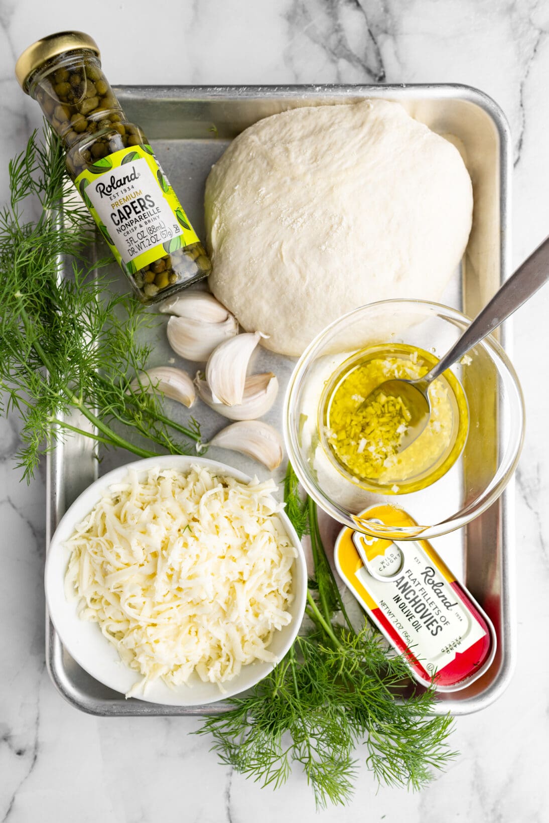 ingredients for anchovy pizza ( cheese, anchovies, garlic, capers, pizza dough, and herbs)