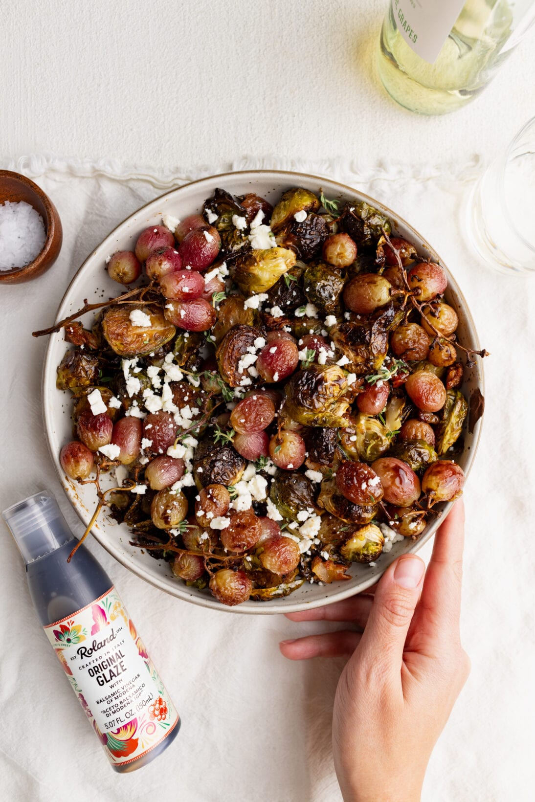 balsamic roasted grapes and Brussels Sprouts in a bowl next to Roland Foods balsamic glaze.