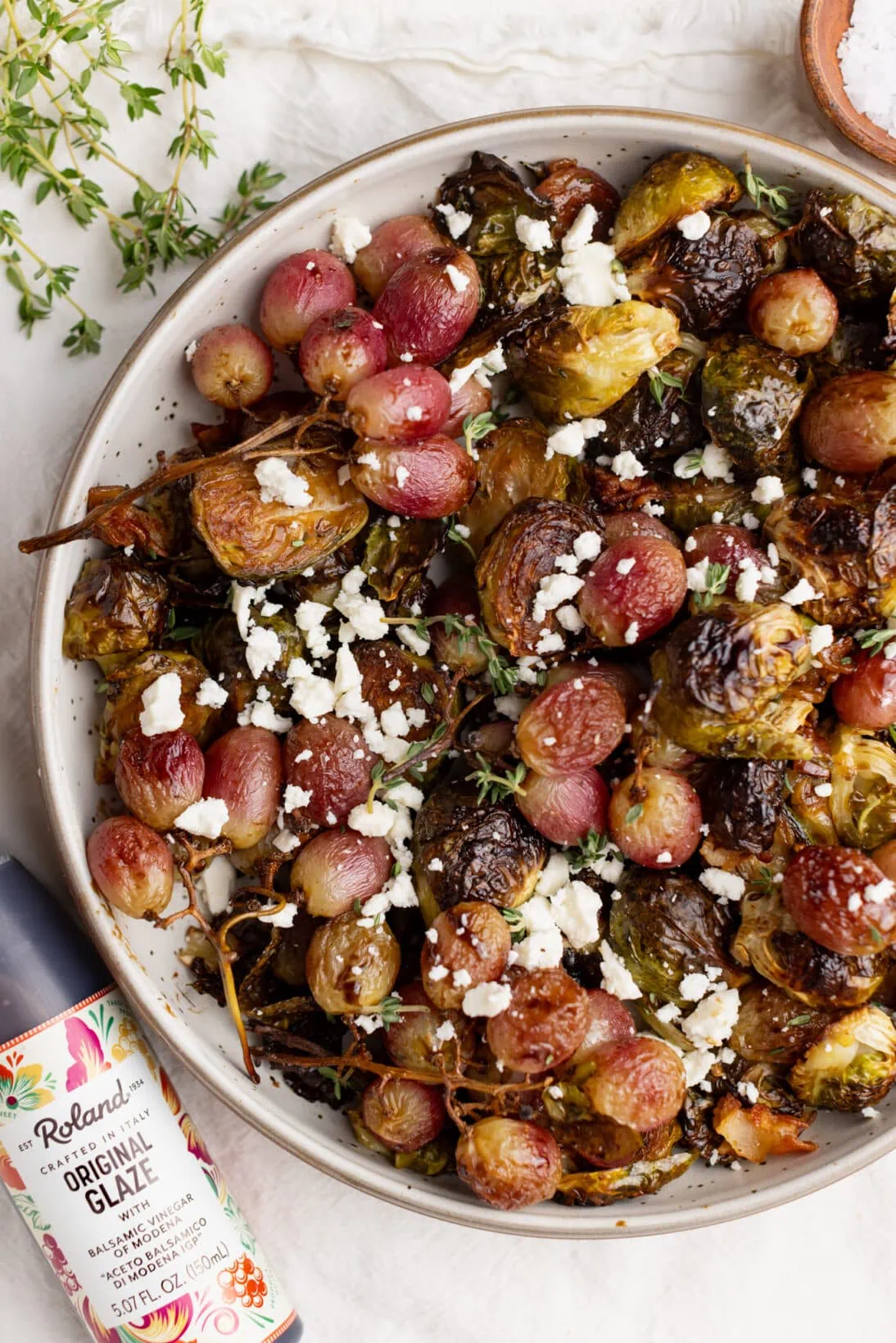 balsamic roasted grapes and Brussels Sprouts in a bowl next to Roland Foods balsamic glaze.