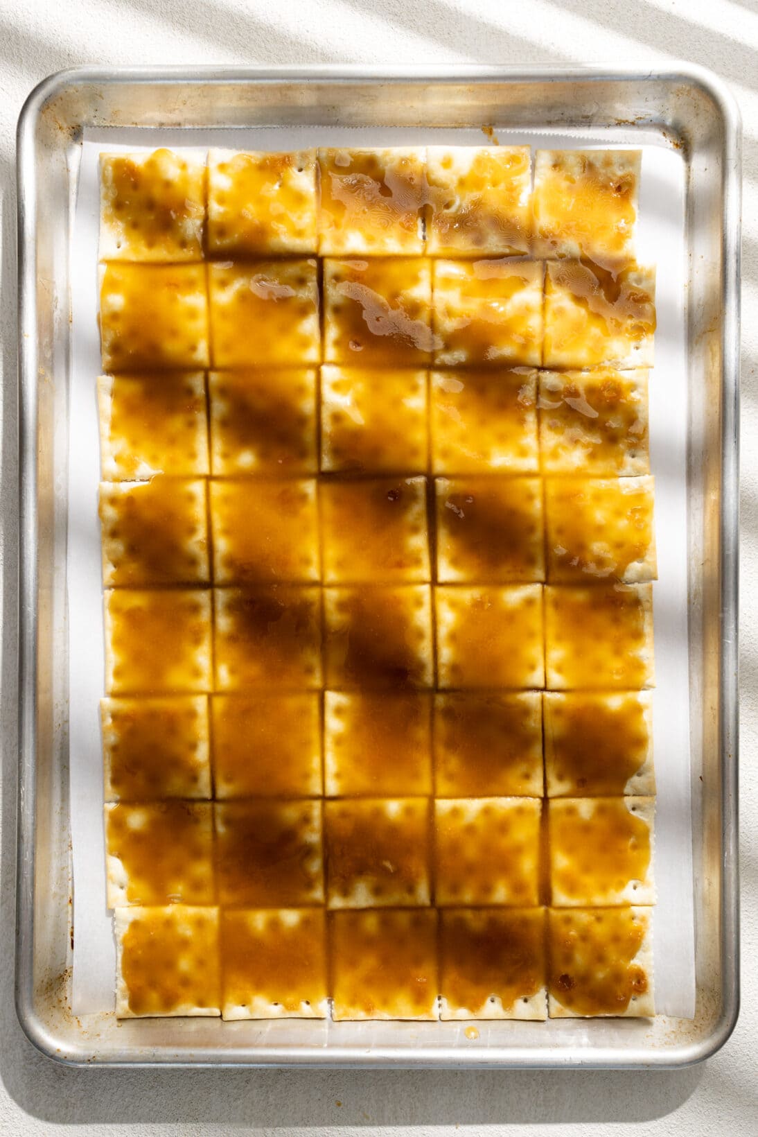 saltines coated in melted toffee laid out on a parchment lined sheet pan