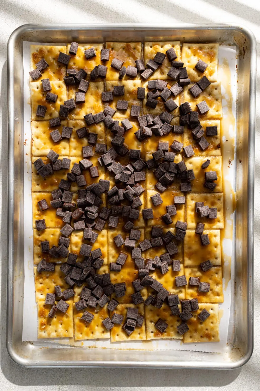 saltines coated in melted toffee topped with chocolate chips laid out on a parchment lined sheet pan