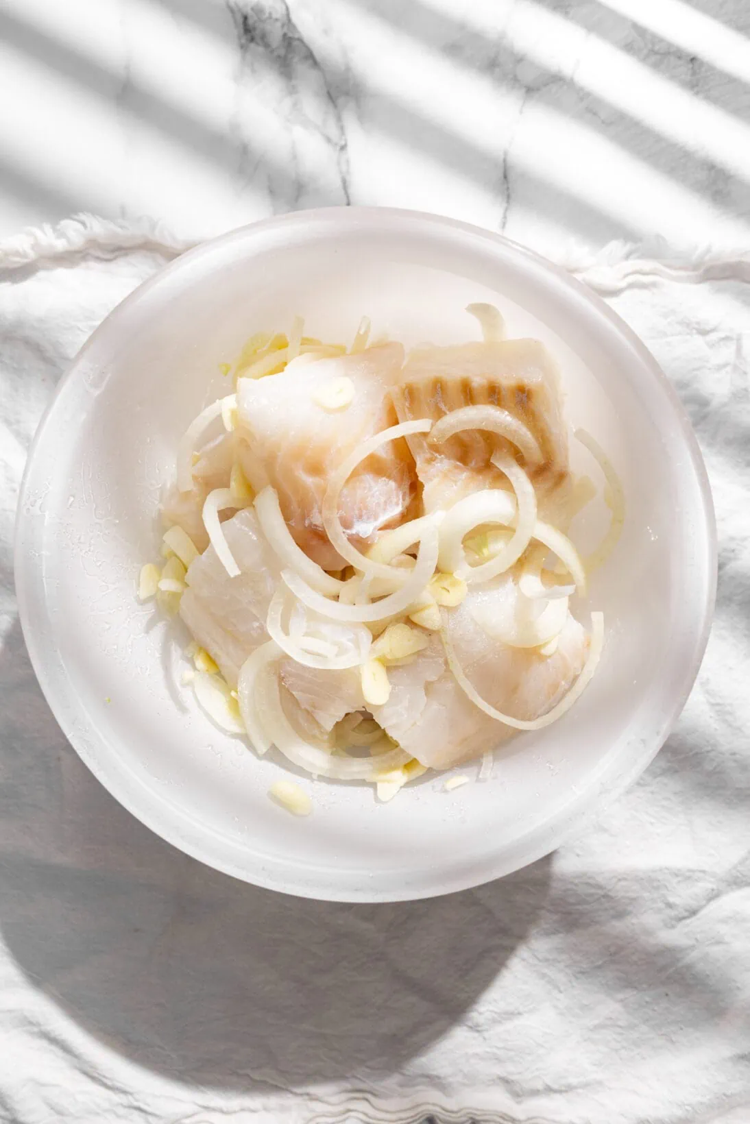cod placed in a bowl with onions, garlic, and salt.