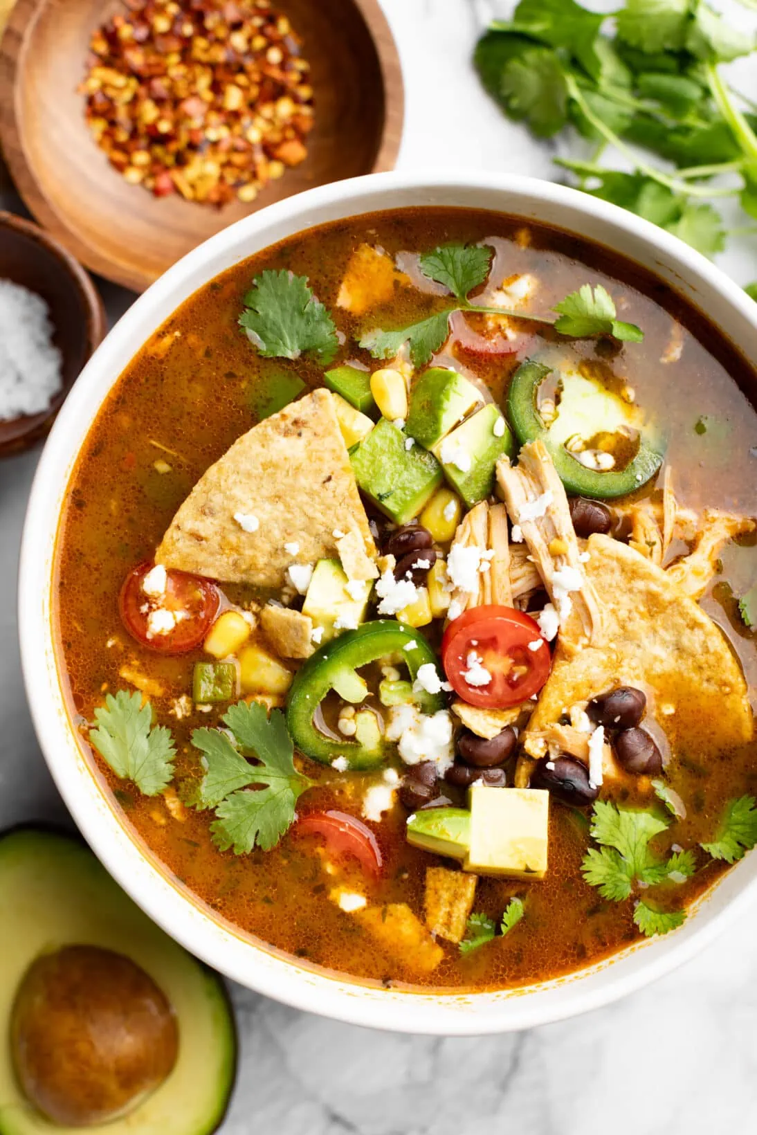bowl of chicken tortilla soup topped with black beans, tortilla chips, tomatoes, chicken, corn, cojita cheese, and cilantro.