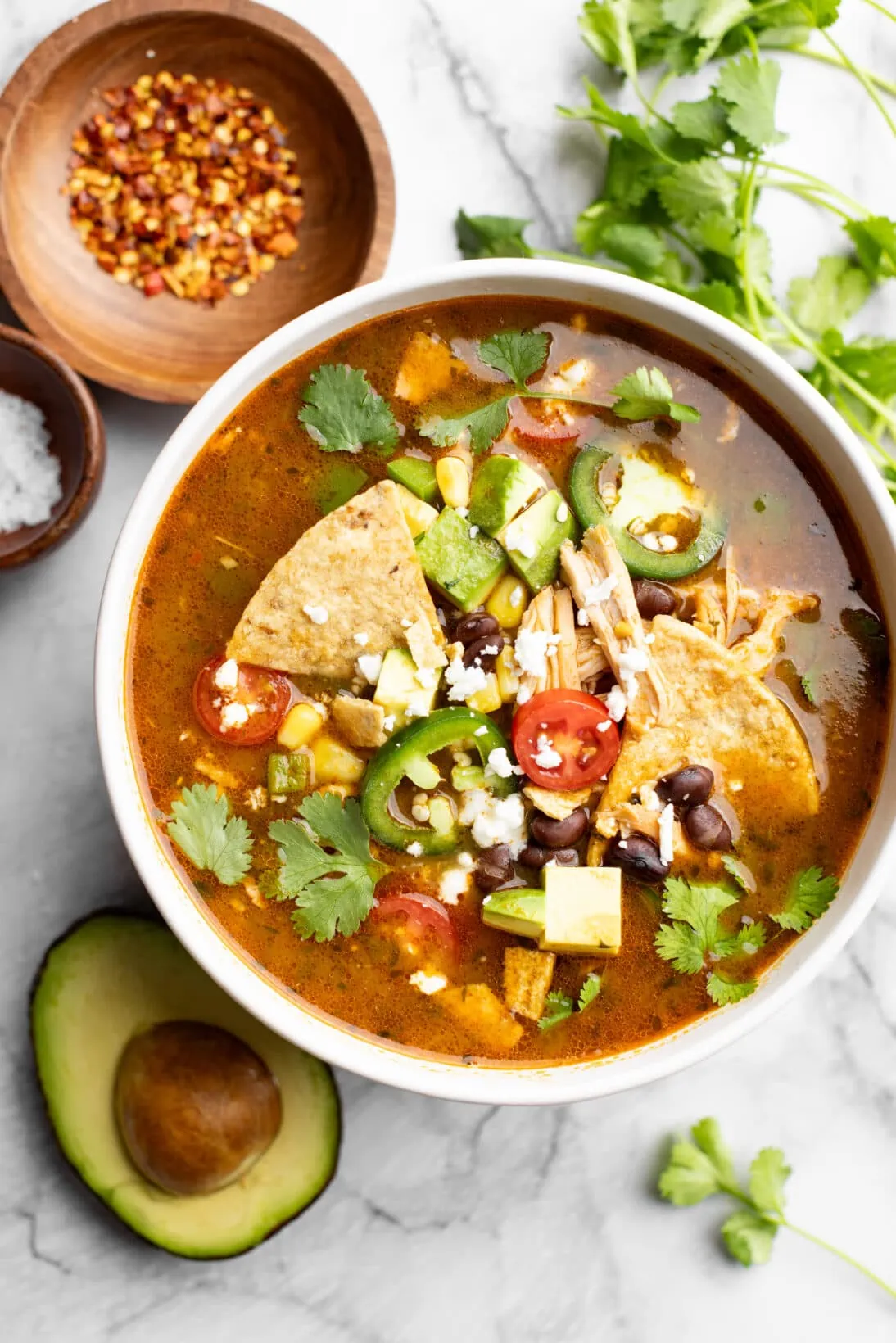 bowl of chicken tortilla soup topped with black beans, tortilla chips, tomatoes, chicken, corn, cojita cheese, and cilantro.