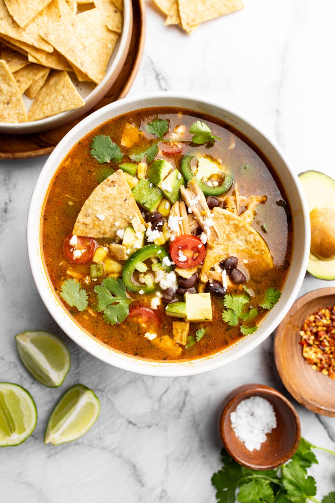 bowl of chicken tortilla soup topped with black beans, tortilla chips, tomatoes, chicken, corn, cojita cheese, and cilantro.