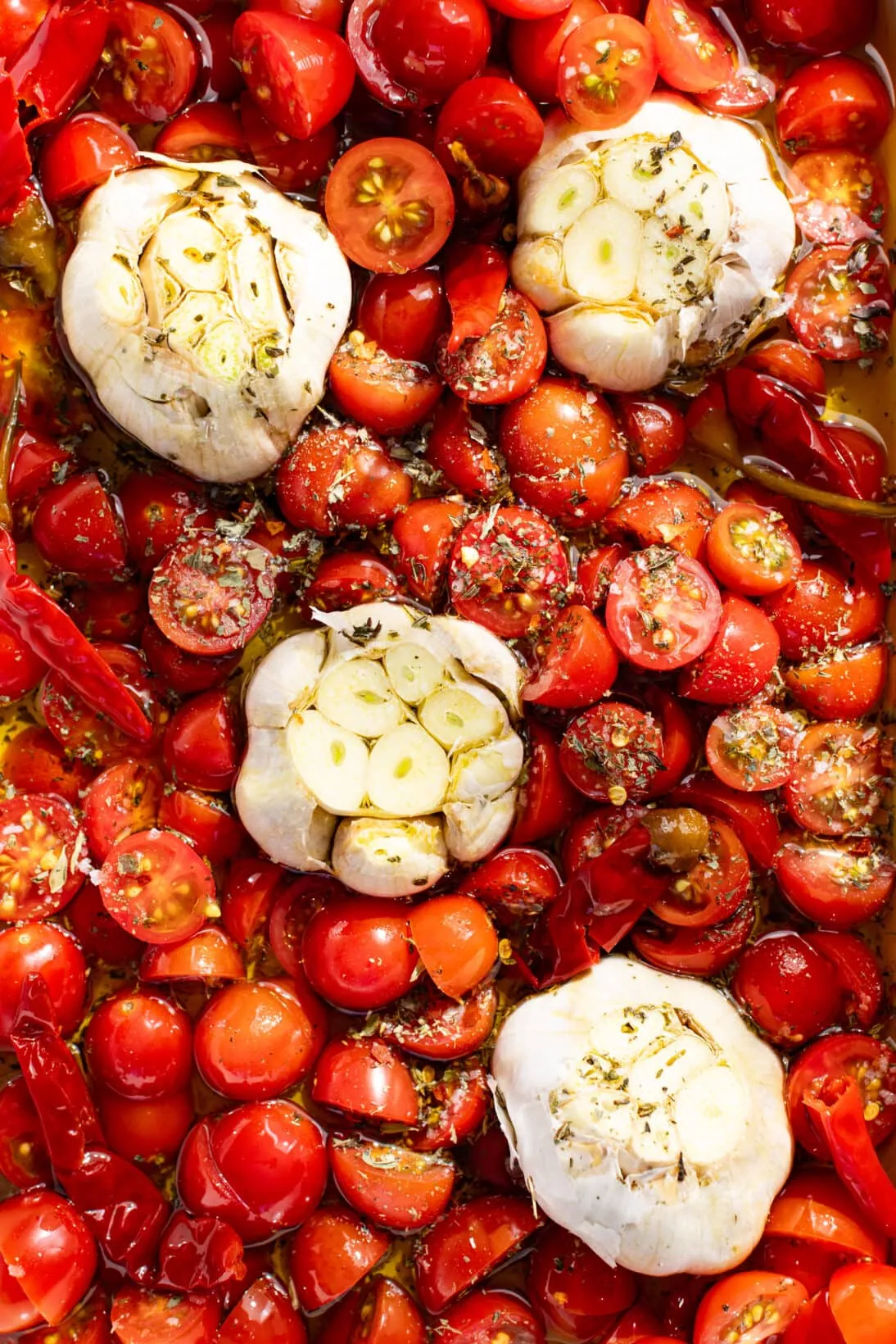 tomatoes, chilies, and heads of garlic in olive oil and dried herbs