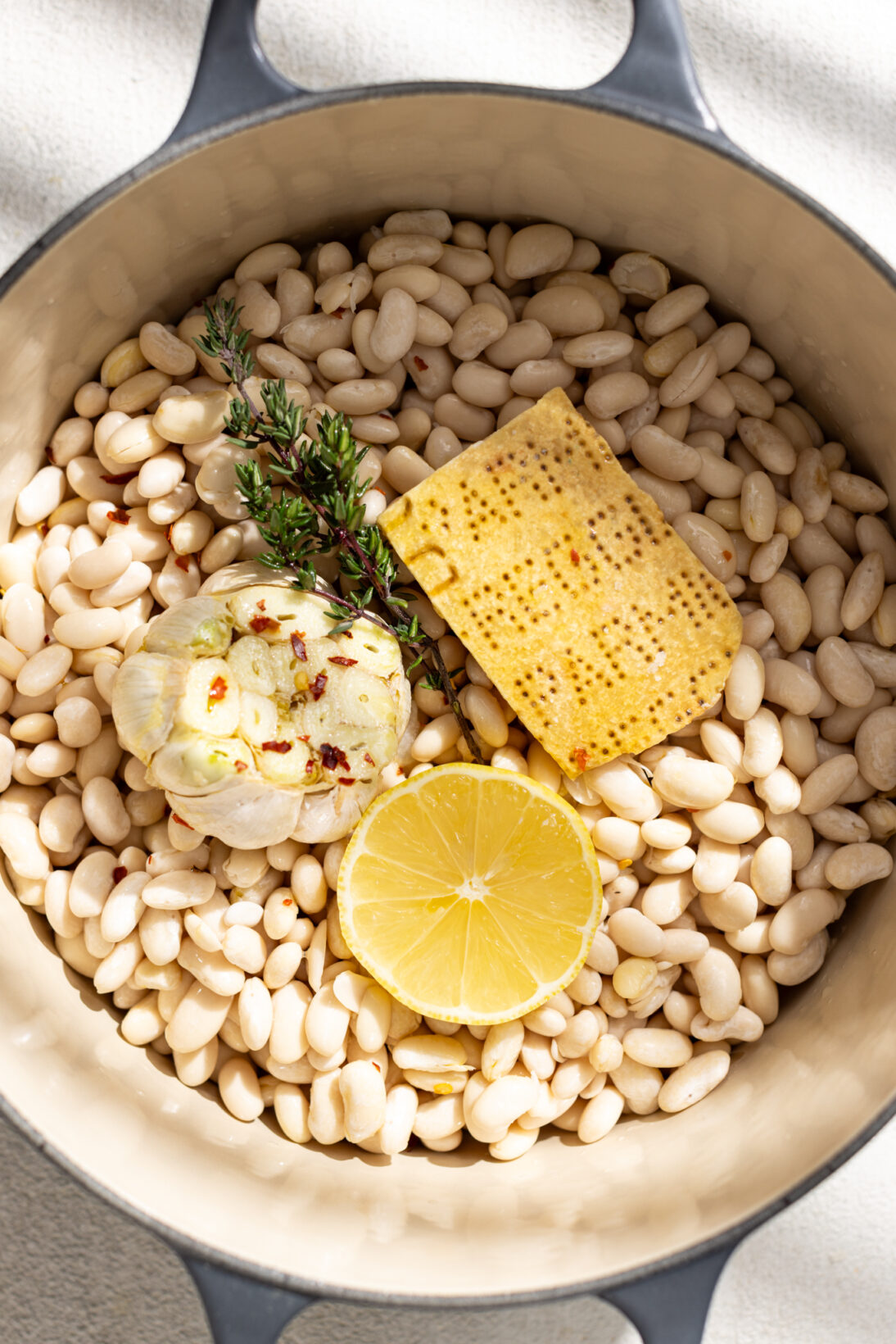 pot of dried hydrated beans, parmesan rind, garlic bulb, thyme, and lemon 