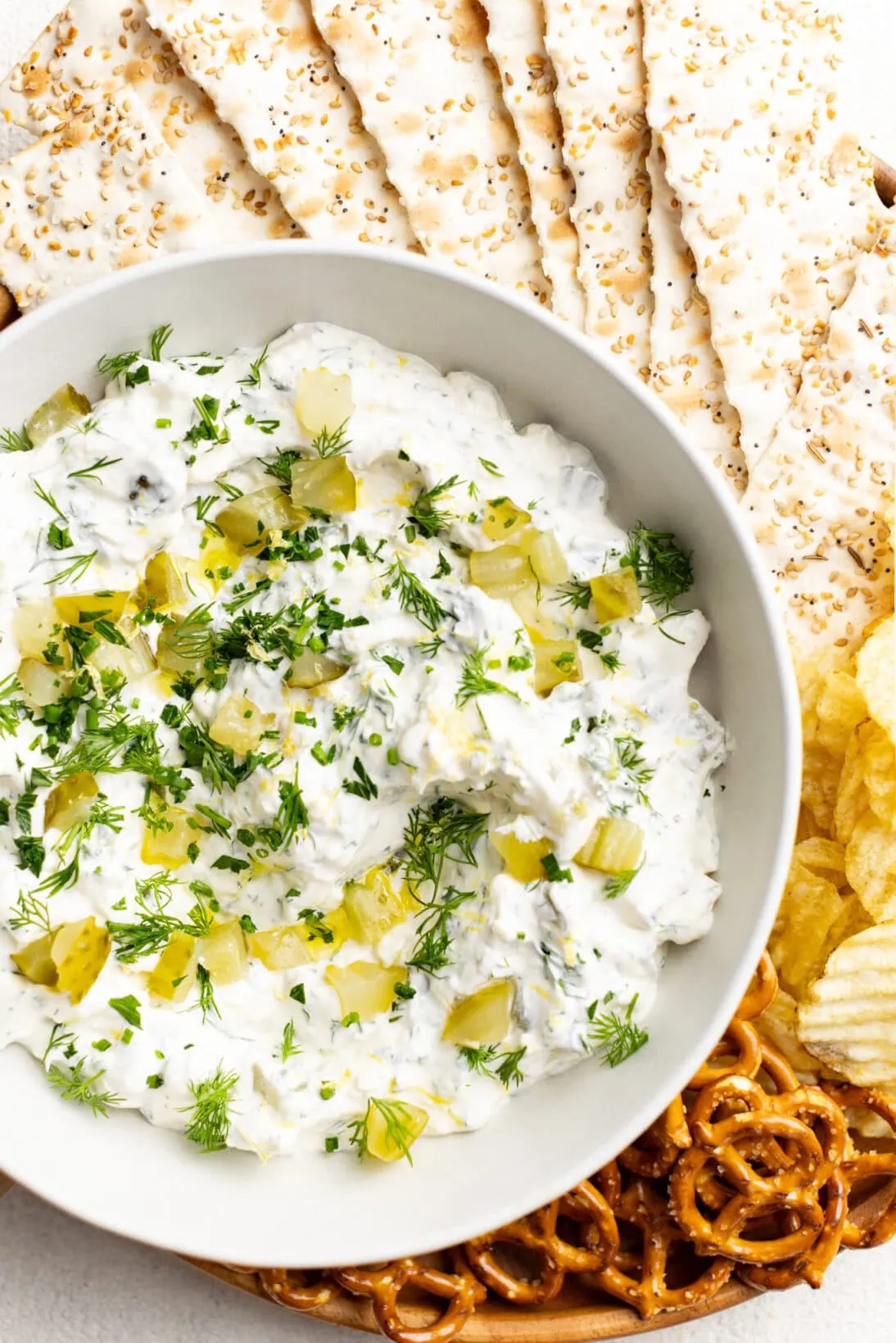 bowl of dill pickle dip surrounded by everything flatbread crackers, chips and pretzels. 