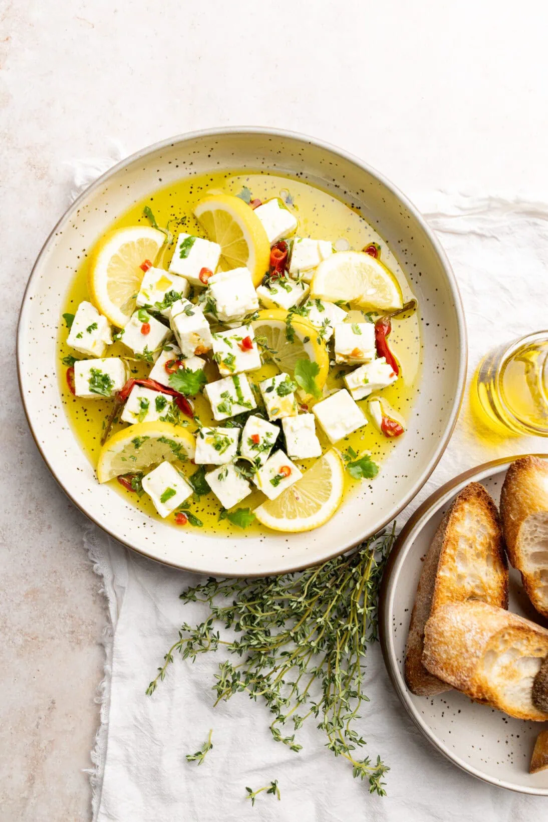 marinated feta on a plate garnished with lemons, next to a plate of crusty bread