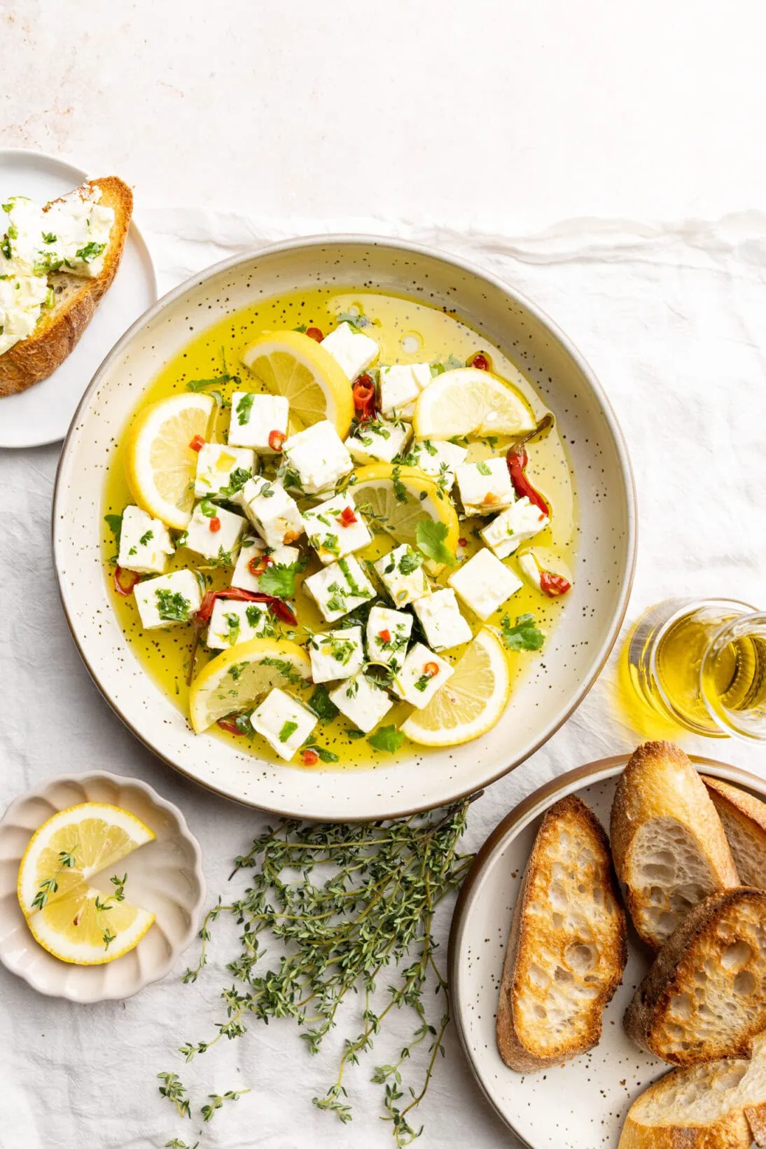 marinated feta on a plate garnished with lemons, next to a plate of crusty bread
