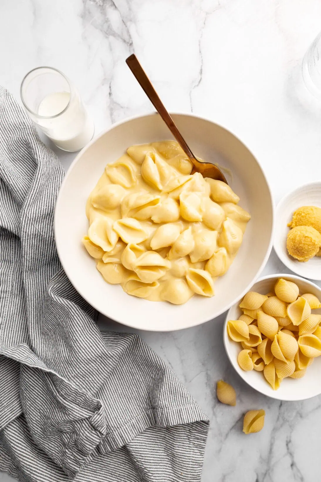 a bowl of roasted garlic miso mac and cheese next to spoonfuls of miso paste and uncooked pasta shells
