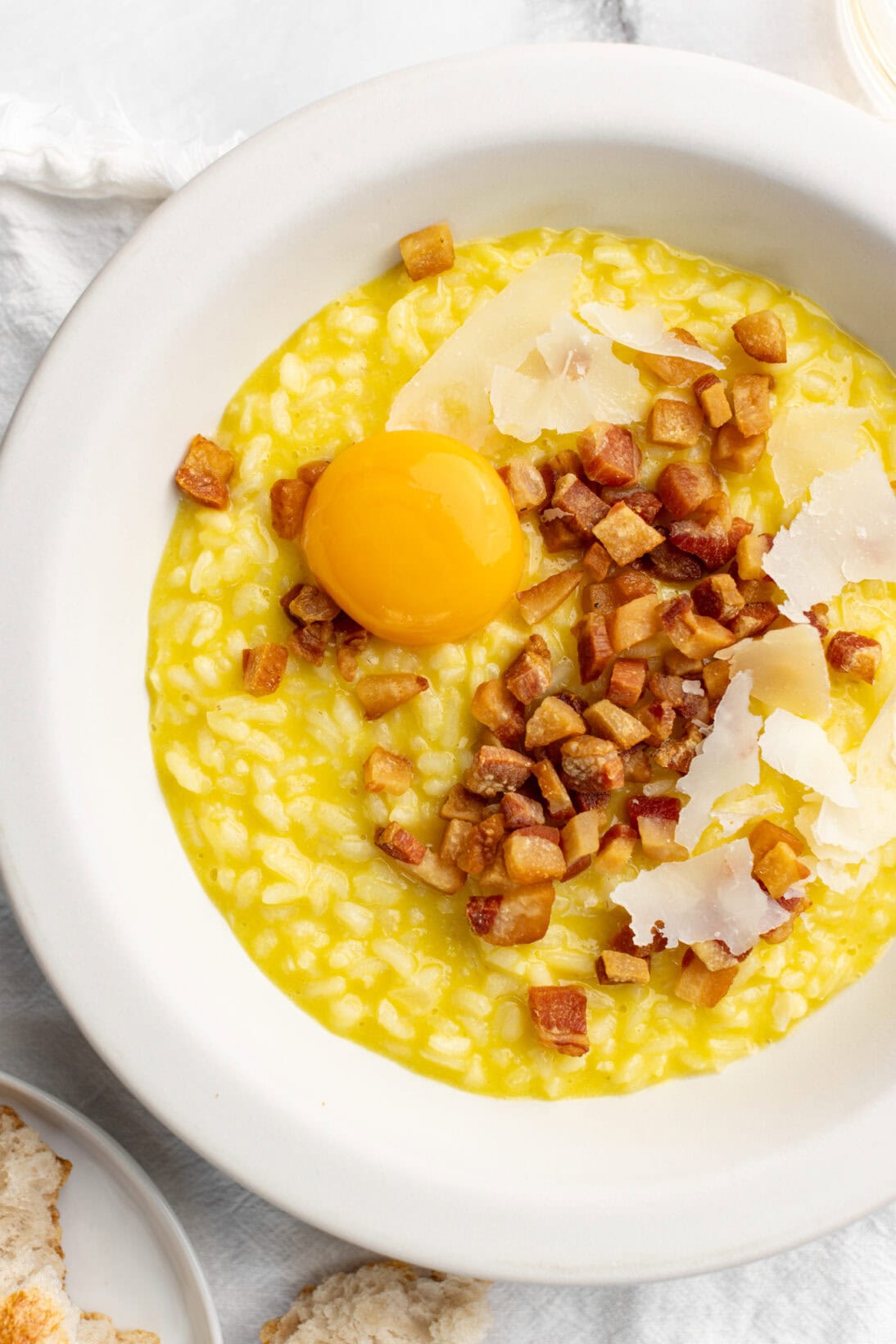 a bowl of risotto carbonara topped with fried guanciale grated cheese and an egg yolk.