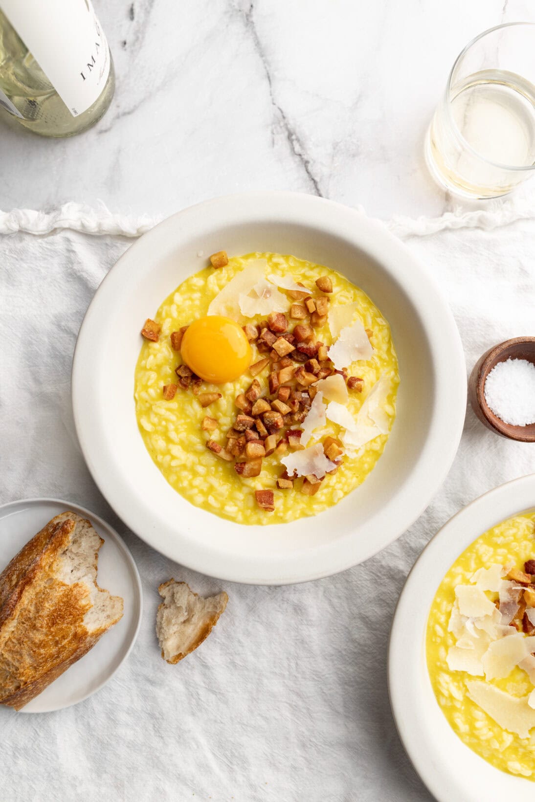 two bowls of risotto carbonara topped with fried guanciale grated cheese and an egg yolk.