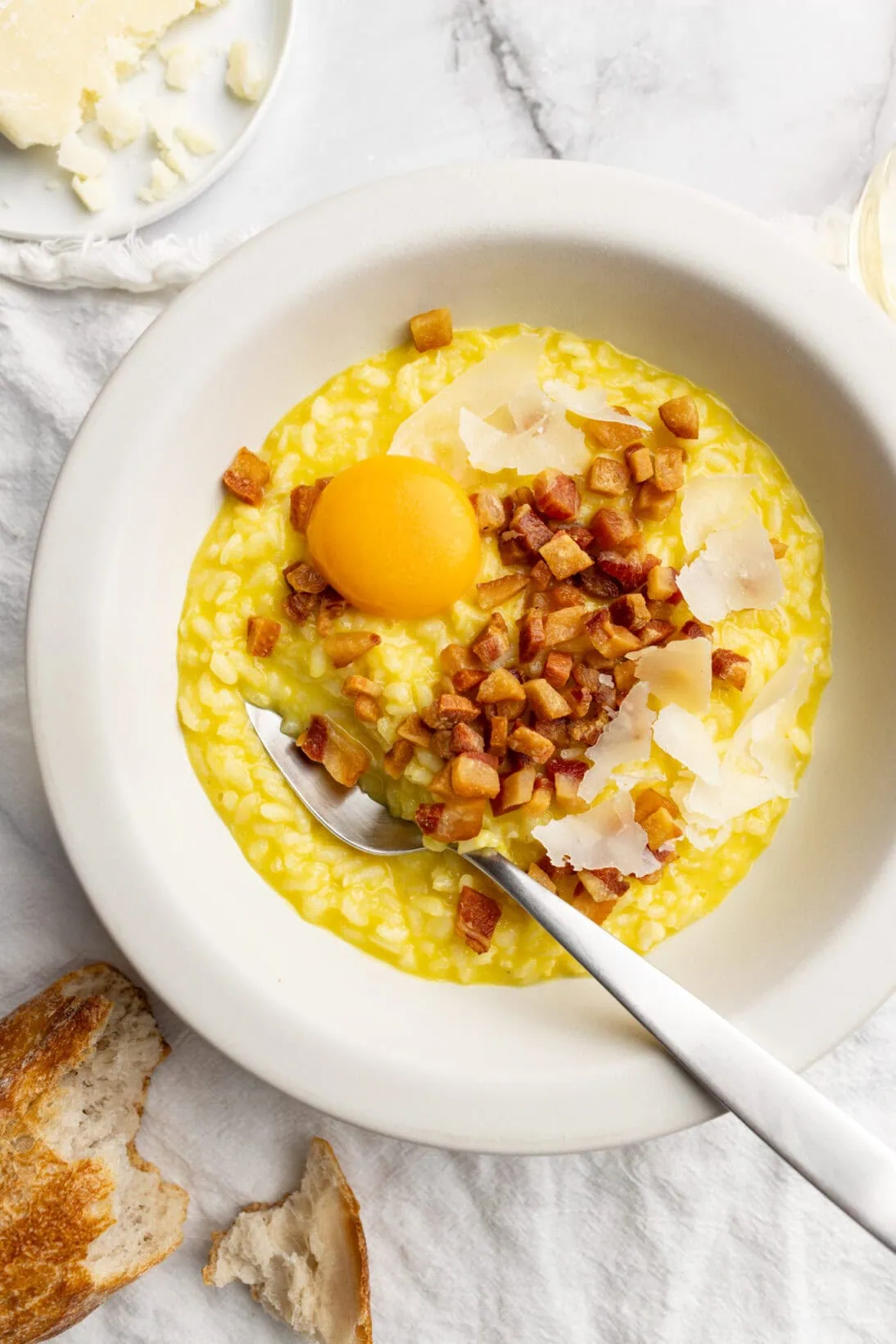 a bowl of risotto carbonara topped with fried guanciale grated cheese and an egg yolk.