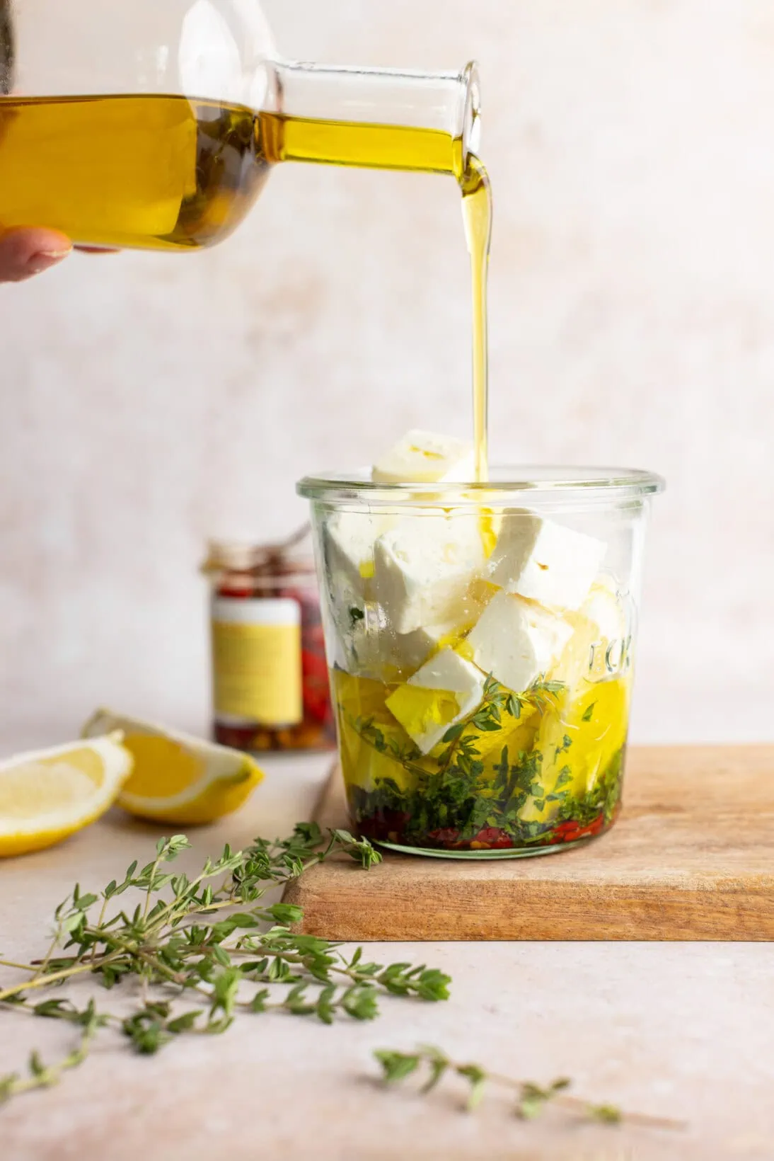 pouring olive oil in a jar with feta herbs and chilies