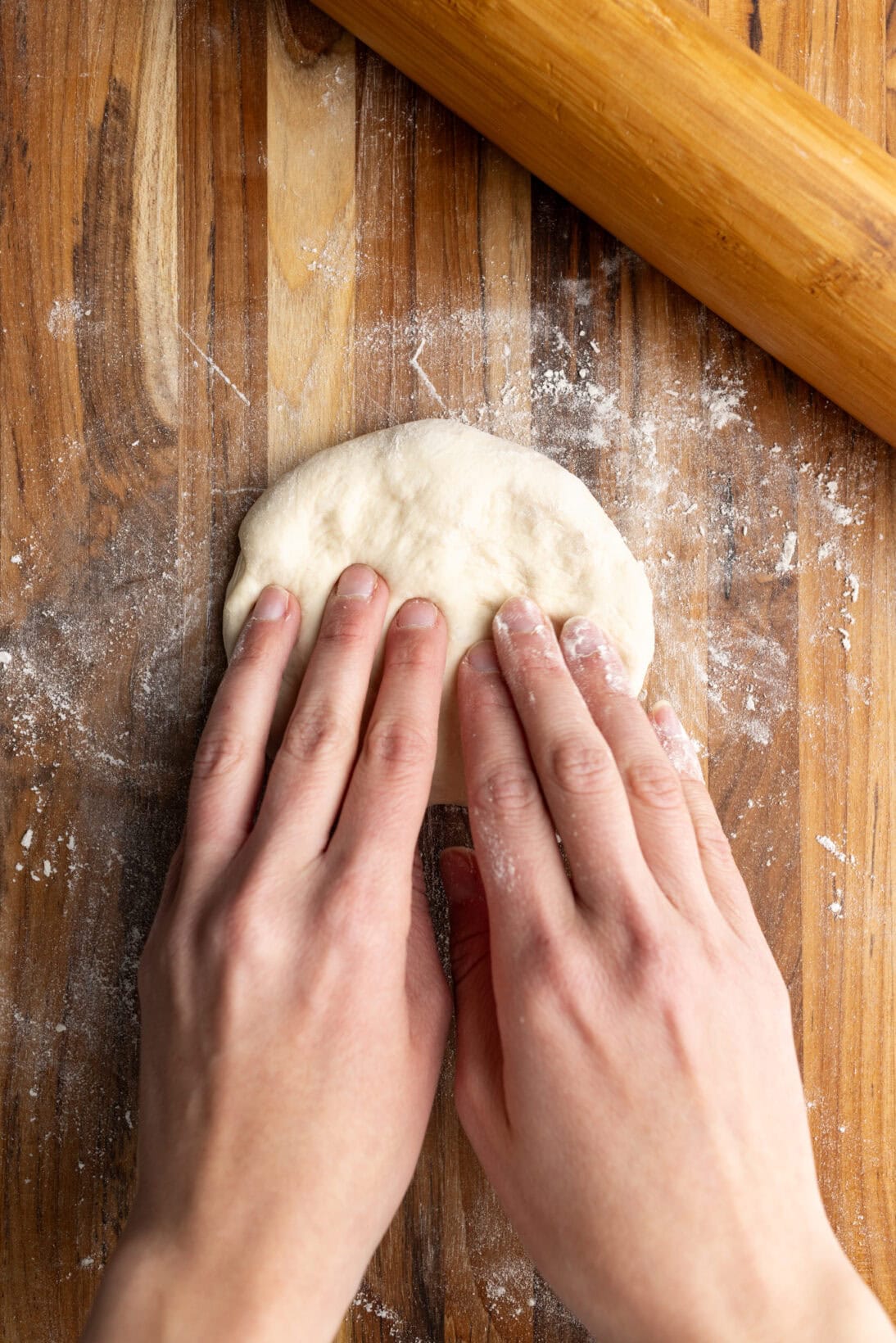 pressing down a rested dough ball to roll out.