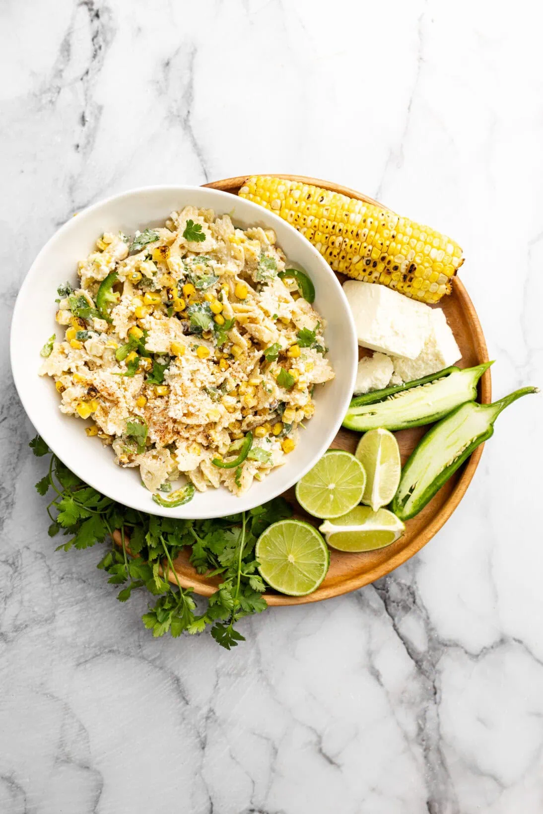 a bowl of Mexican street corn pasta salad next to the ingredients that go into it.