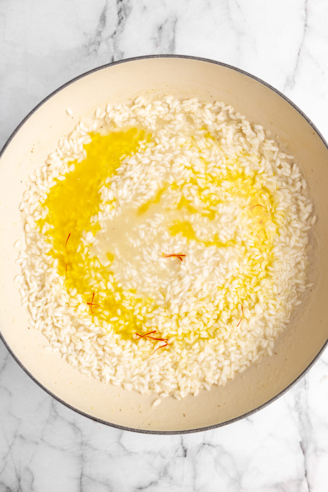 cooking risotto alla milanese - adding the saffron broth to the rice midway cook