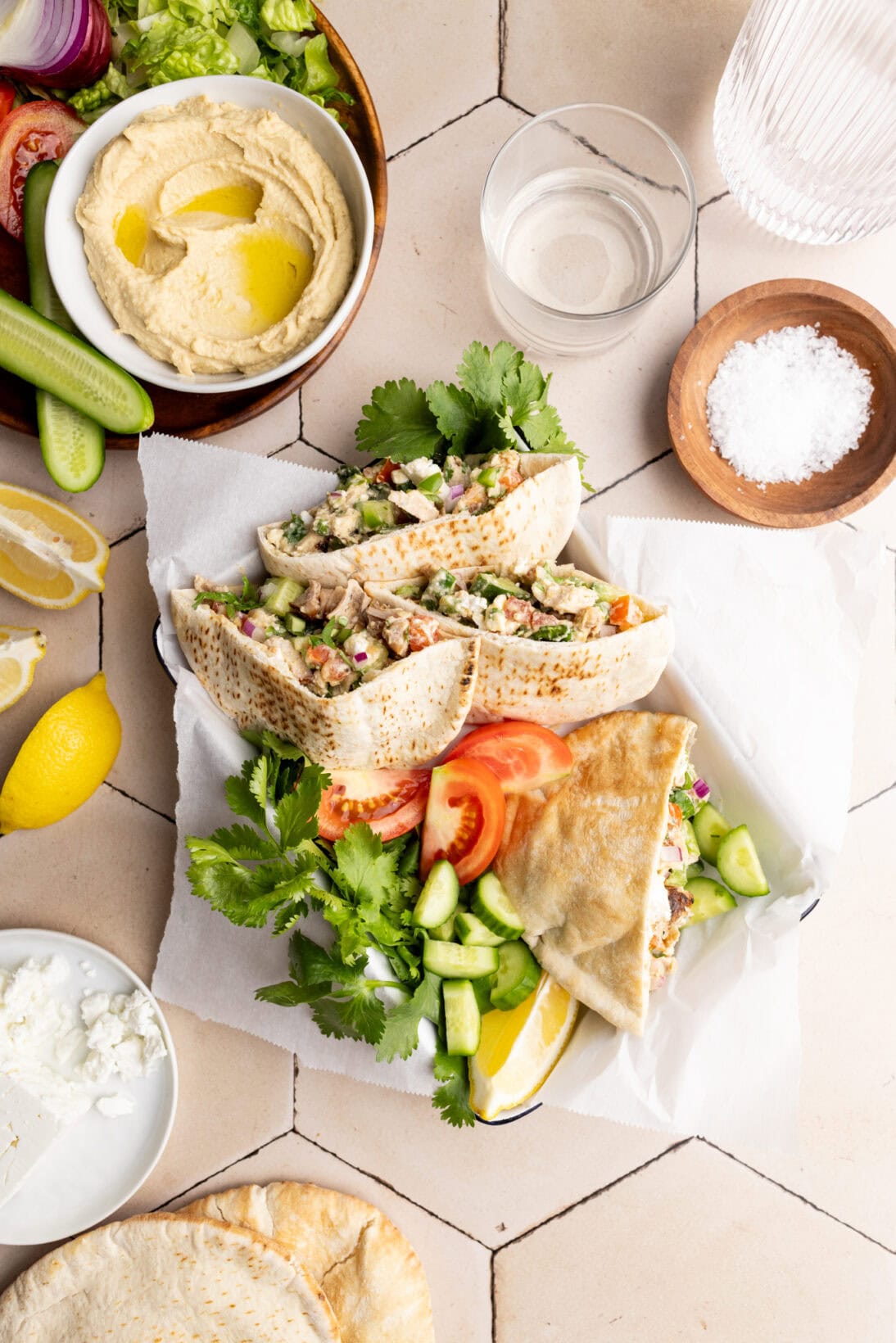 a tray of pita bread stuffed with hummus chicken salad. Also in the tray is bunches of cilantro, tomatoes, and lemon.

Nest to the tray is a plate with all the ingredients that go into the salad. 