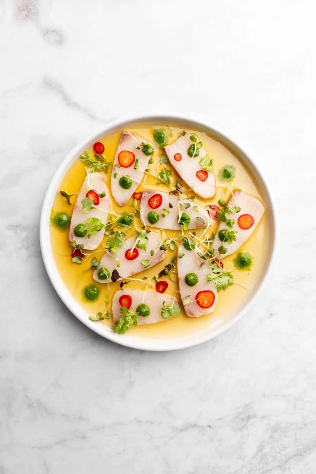 Hamachi crudo plated with chilies, jalapeno and cilantro puree and micro greens.
