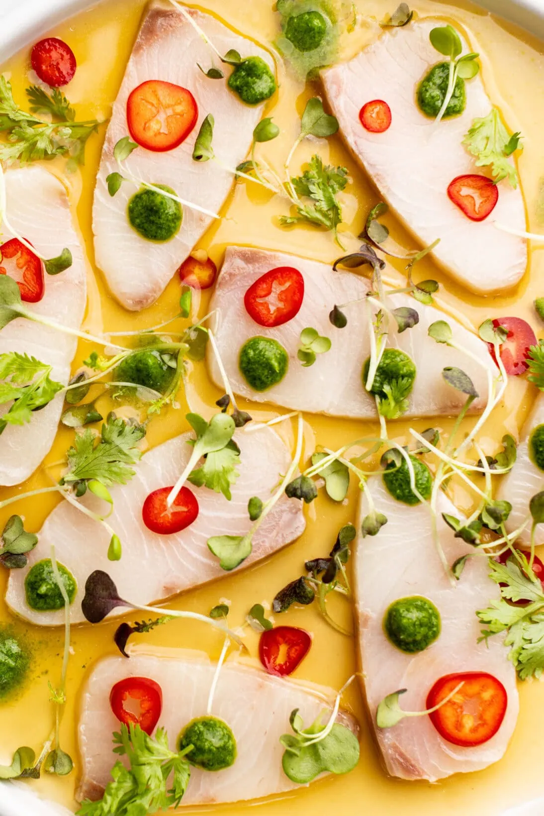up close Hamachi crudo plated with chilies, jalapeno and cilantro puree and micro greens
