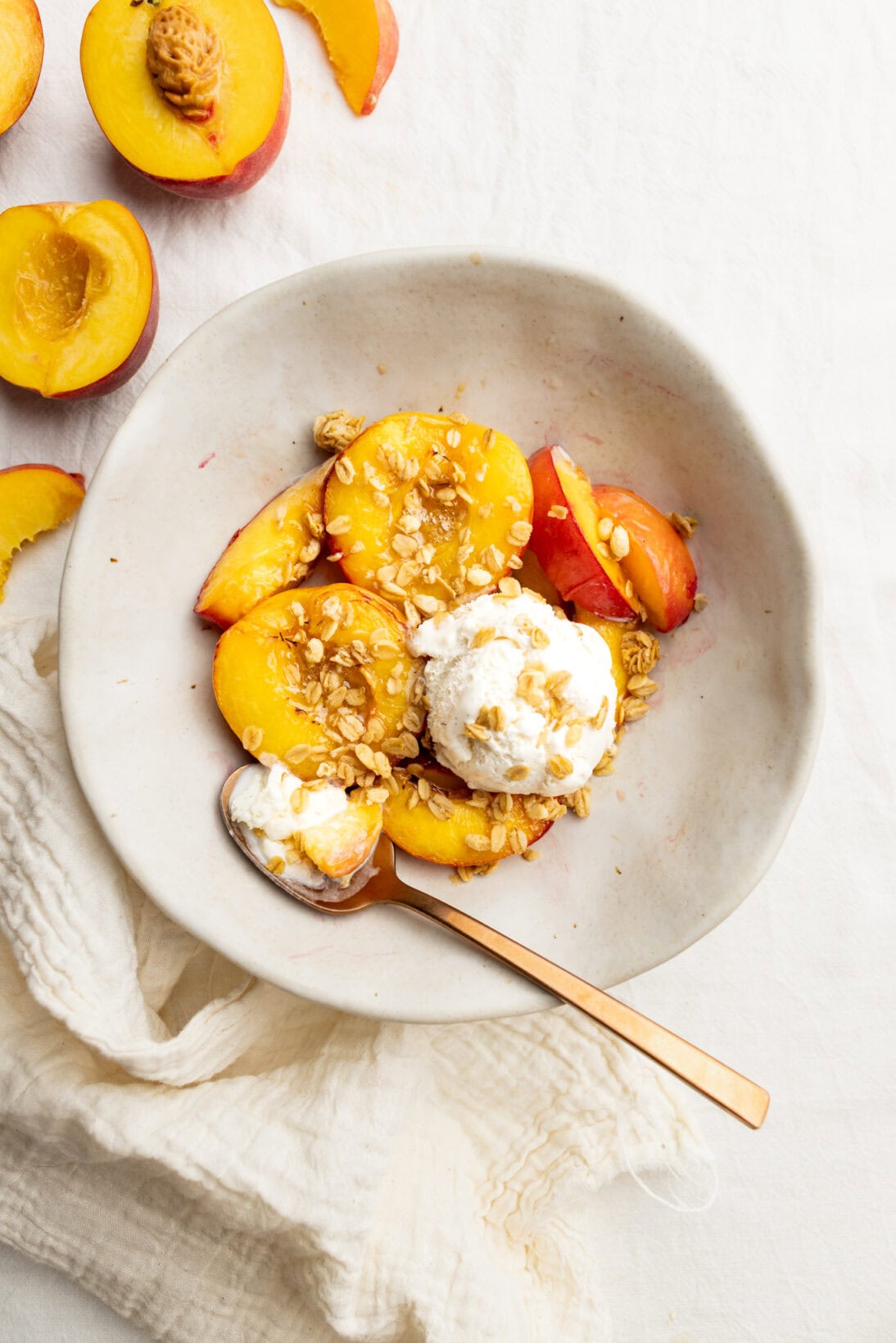 a bowl of sir fryer peaches topped with melty vanilla ice cream and granola clusters.