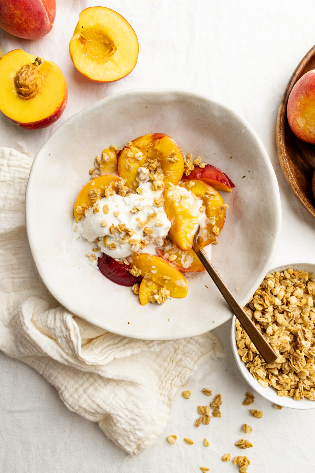 a bowl of sir fryer peaches topped with melty vanilla ice cream and granola clusters.