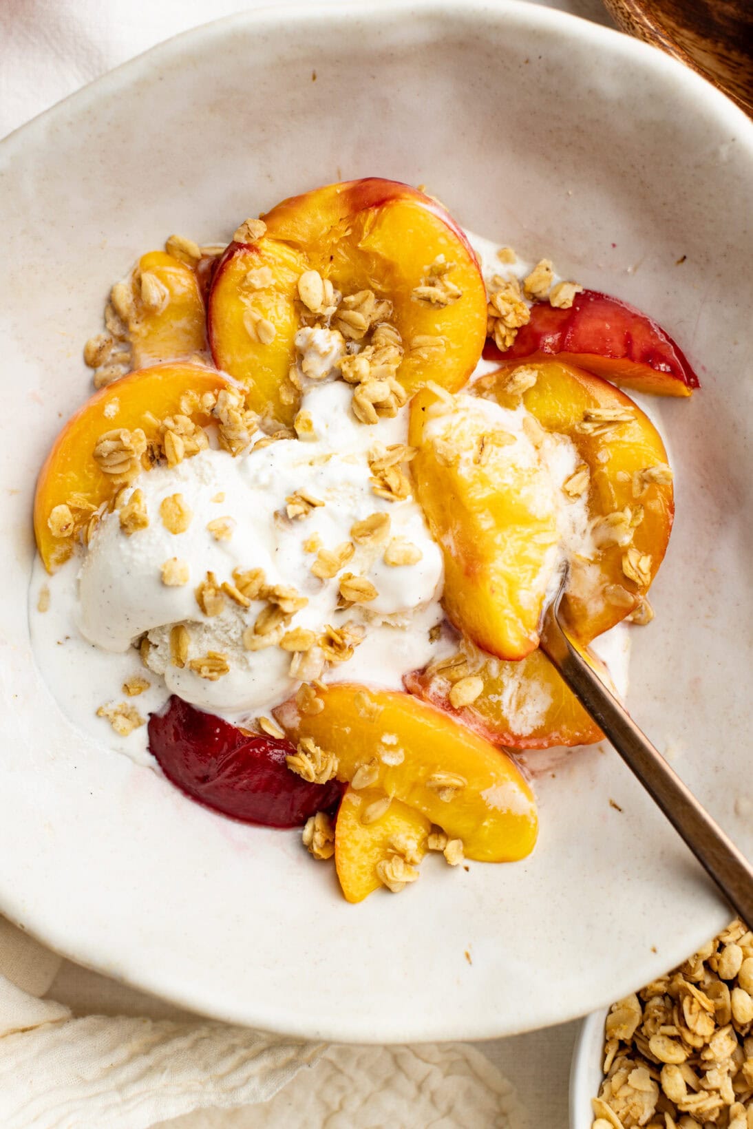 a bowl of air fryer peaches topped with melty vanilla ice cream and granola clusters.