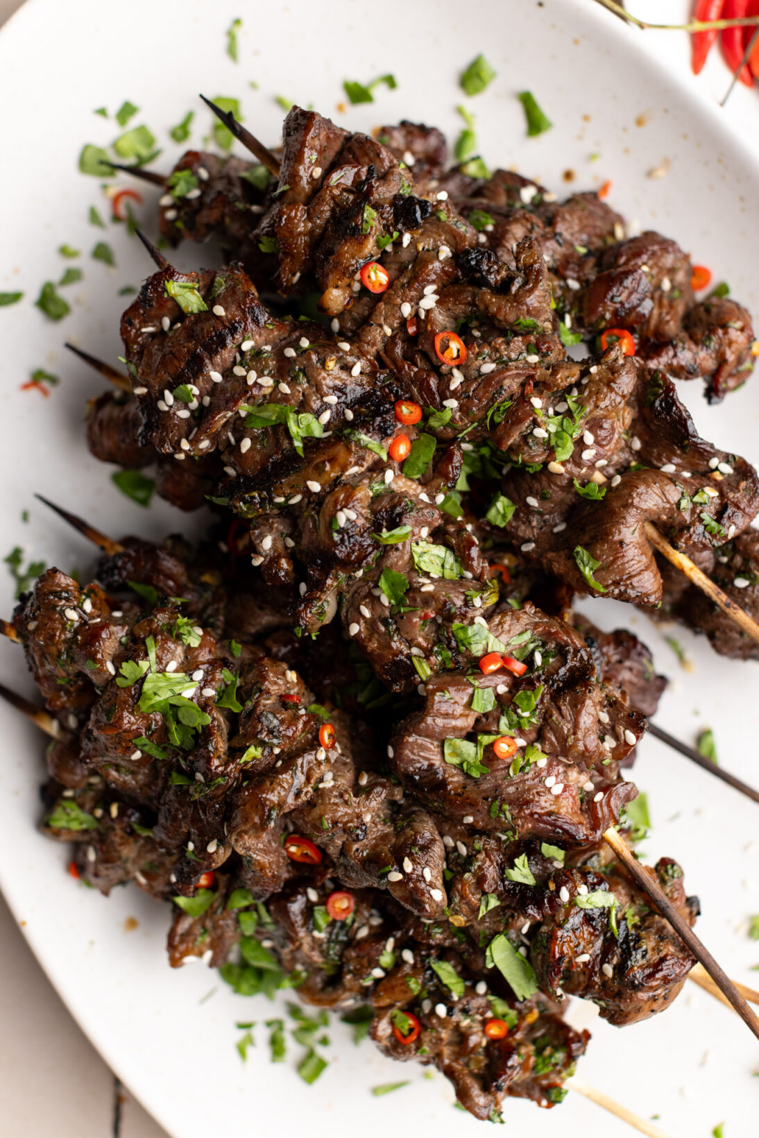 cooked beef satay skewers topped with sesame seeds, cilantro, and extra chilies.