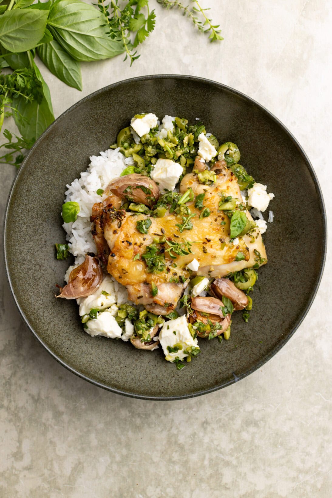 herb roasted chicken thigh in a bowl over rice, topped with a green olive and herb dressing.