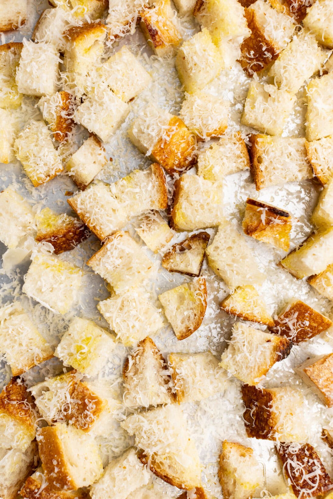 cut sourdough bread placed on a sheet tray, seasoned, and covered in Parmesan cheese