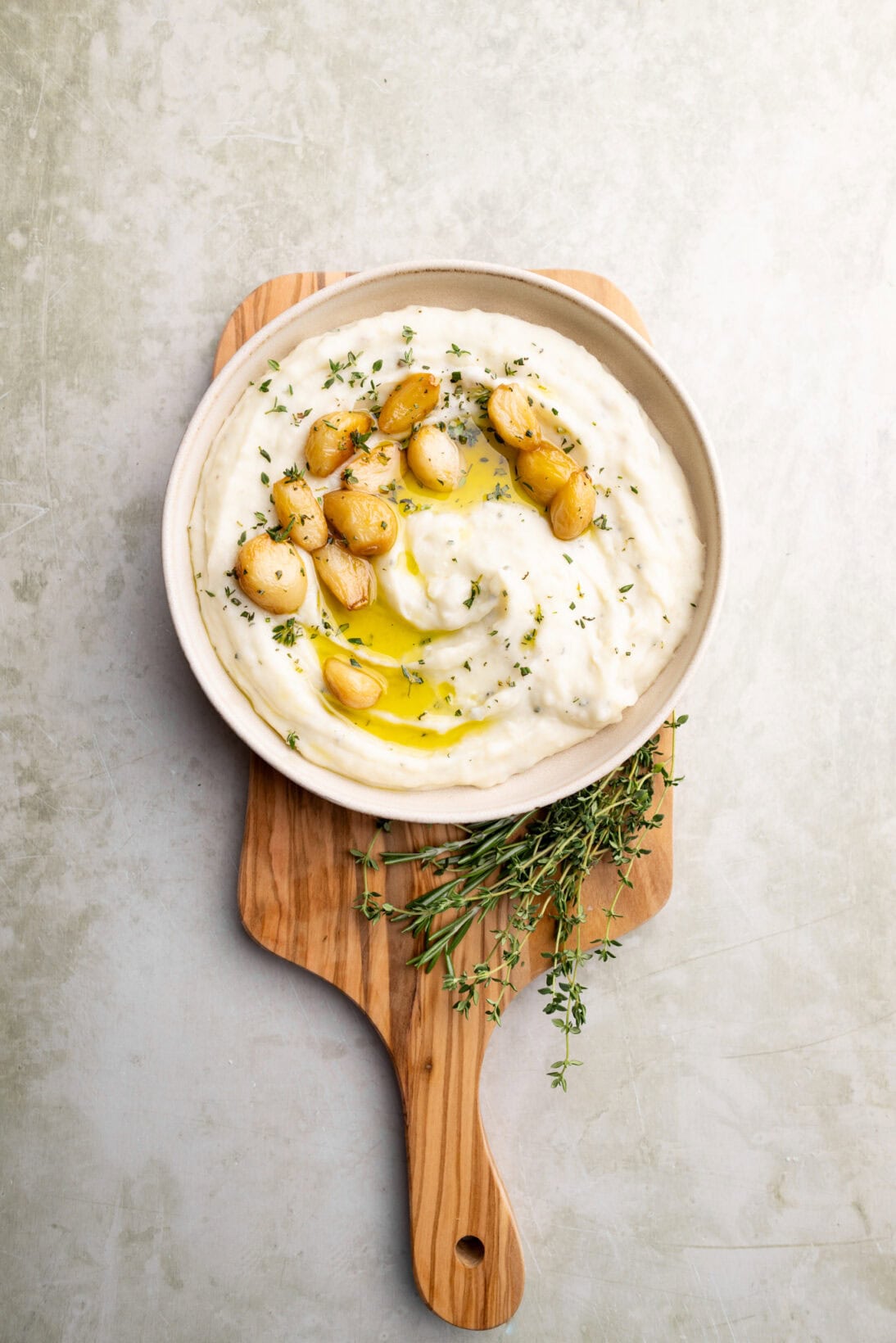 garlic and herb mashed potatoes with extra garlic confit on top on a wooden cutting board