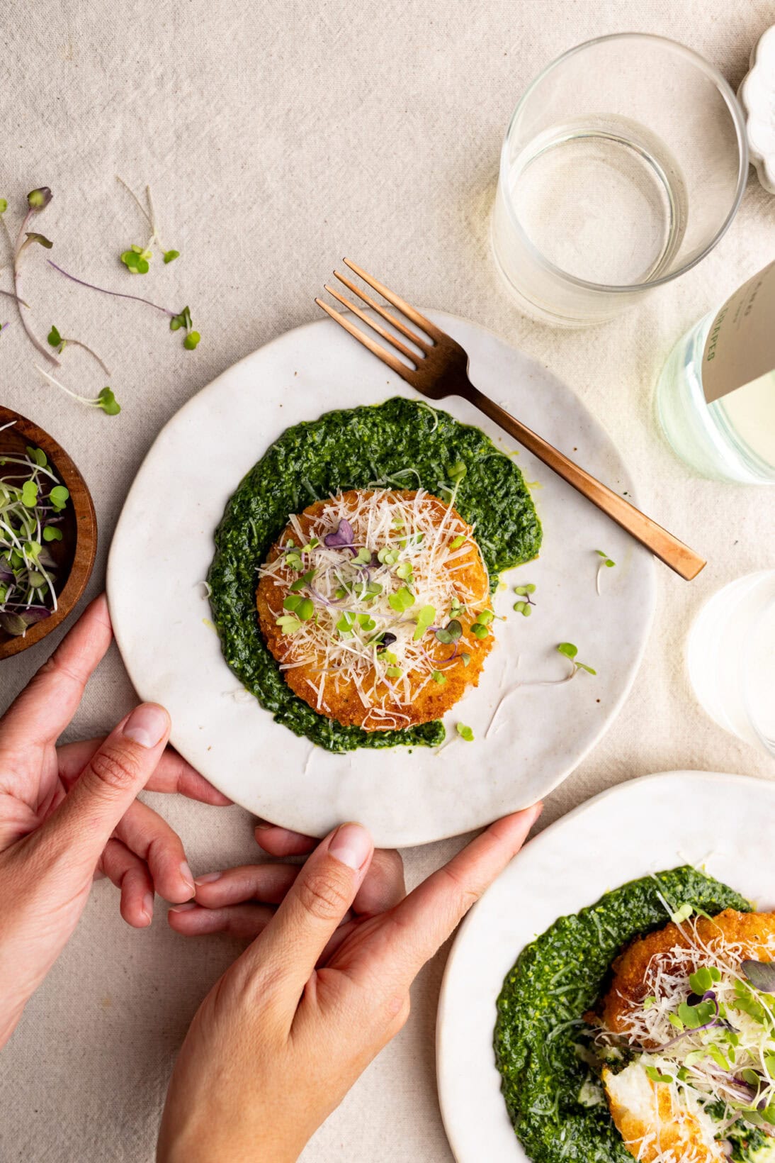 2 plates of risotto cakes topped with parmesan cheese over a generous helping of spinach pesto
