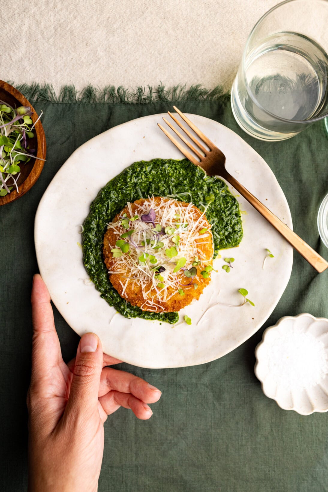 a plate of risotto cakes topped with parmesan cheese over a generous helping of spinach pesto