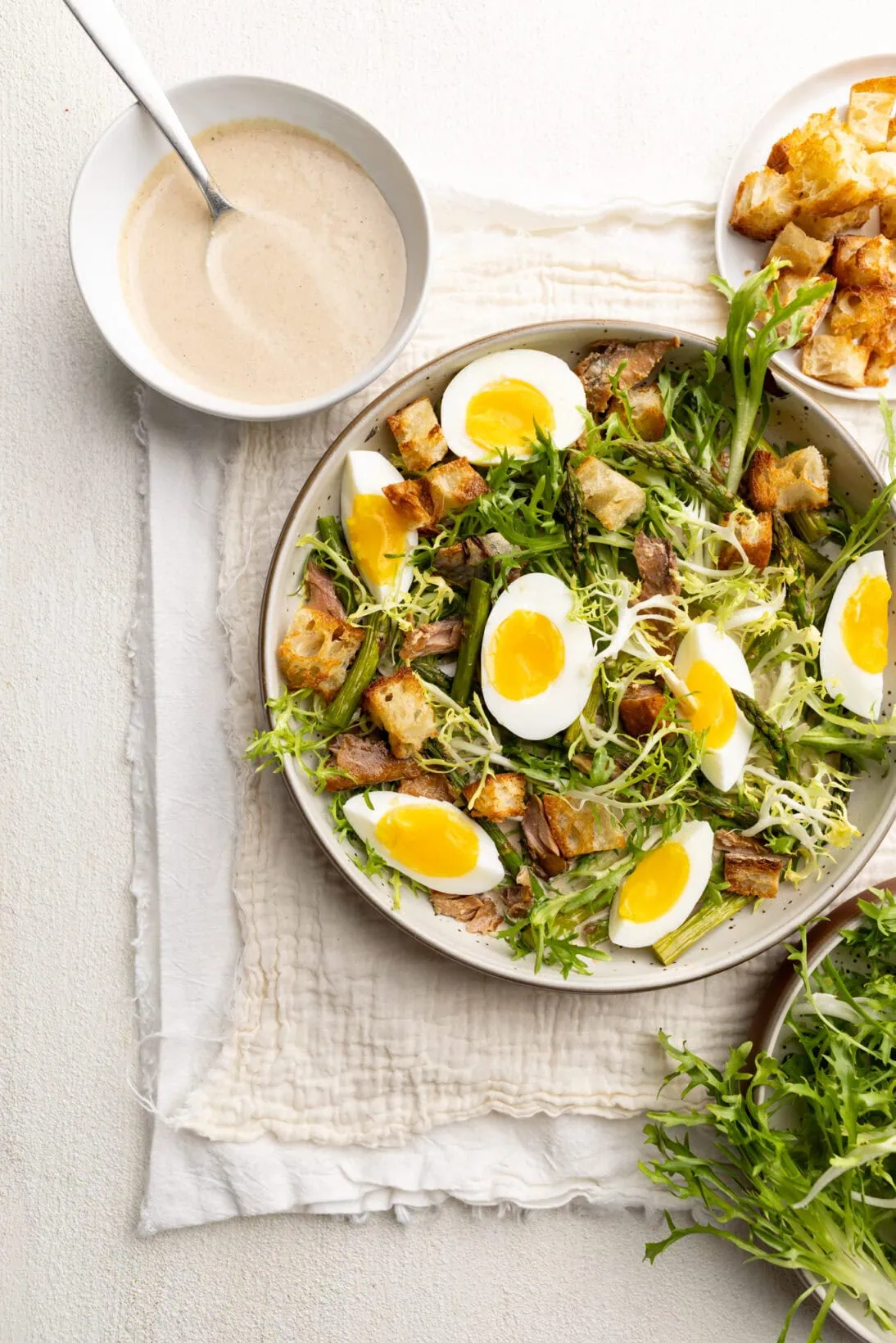 a frisée, roasted asparagus, jammy eggs, and croutons salad served over a layer of tonnato sauce.