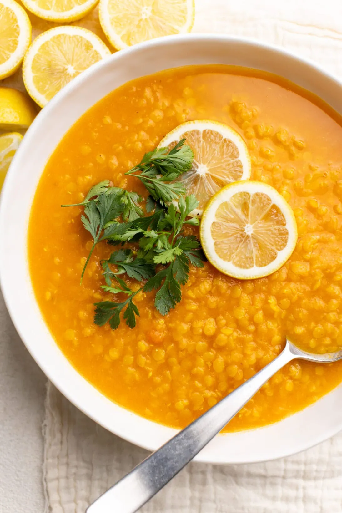 a bowl of Lebanese carrot lentil soup on the side of lemons. 