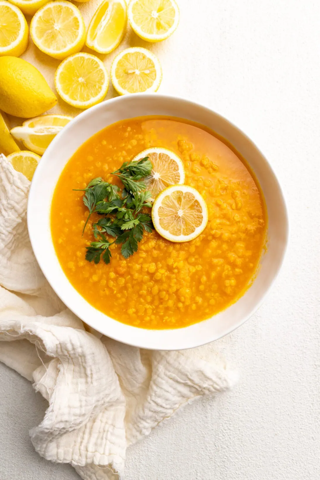 a bowl of Lebanese carrot lentil soup on the side of lemons. 