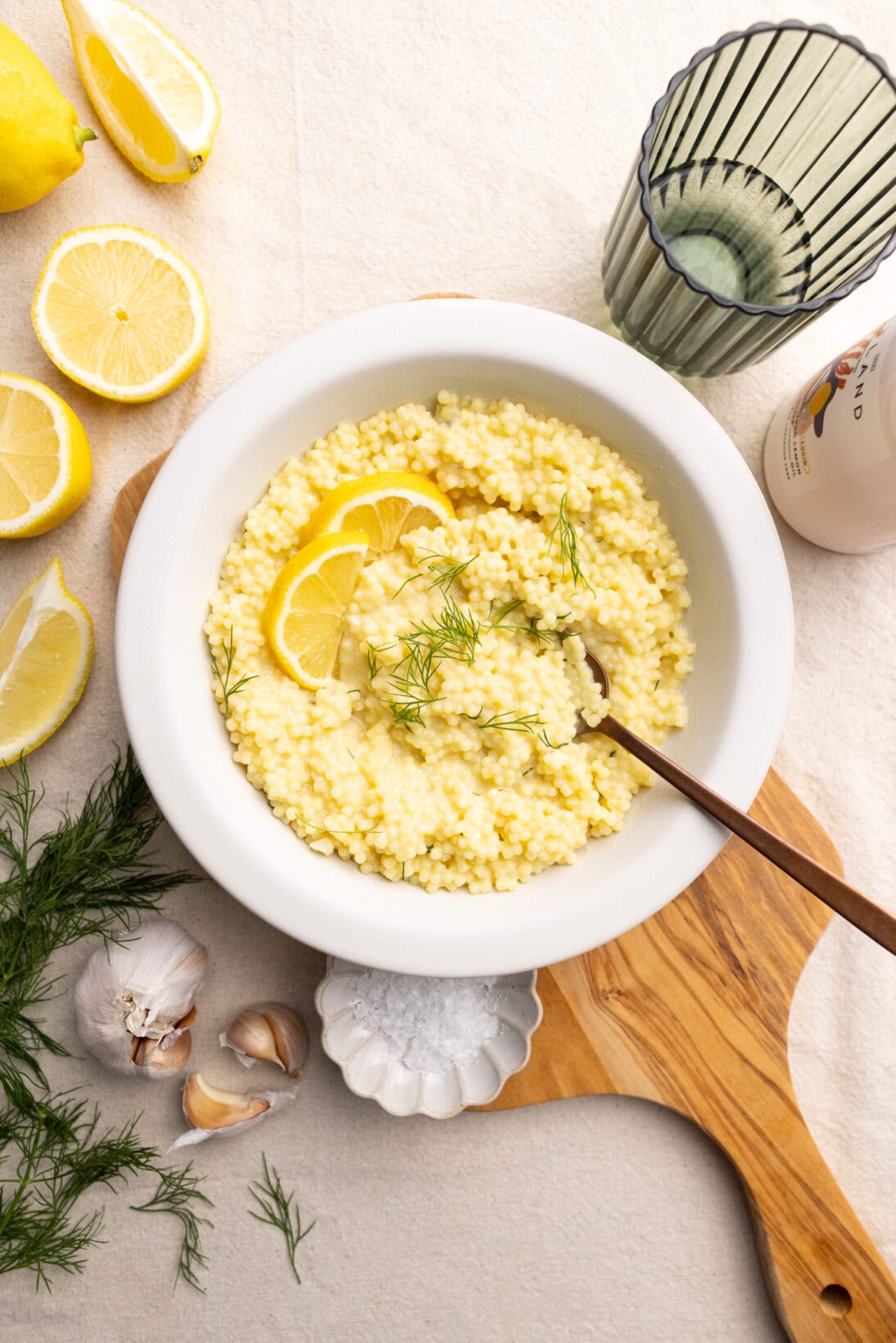 A bowl of lemon pastina on a wooden serving board garnished with lemon and dill. 