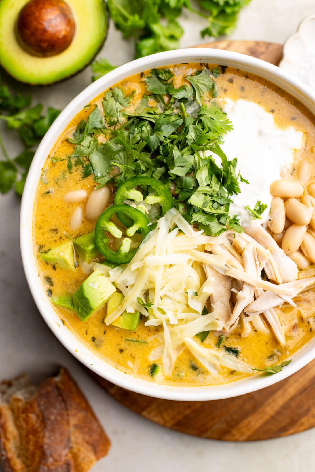 A bowl of white bean chicken chili topped with cheese, sour cream, and avocado. 