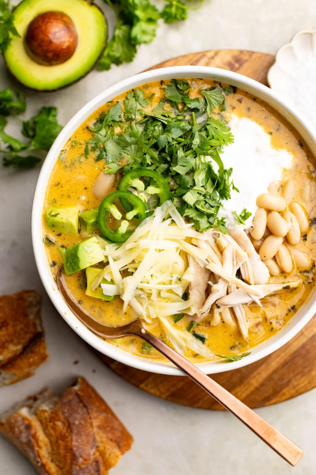 A bowl of white bean chicken chili topped with cheese, sour cream, and avocado. 