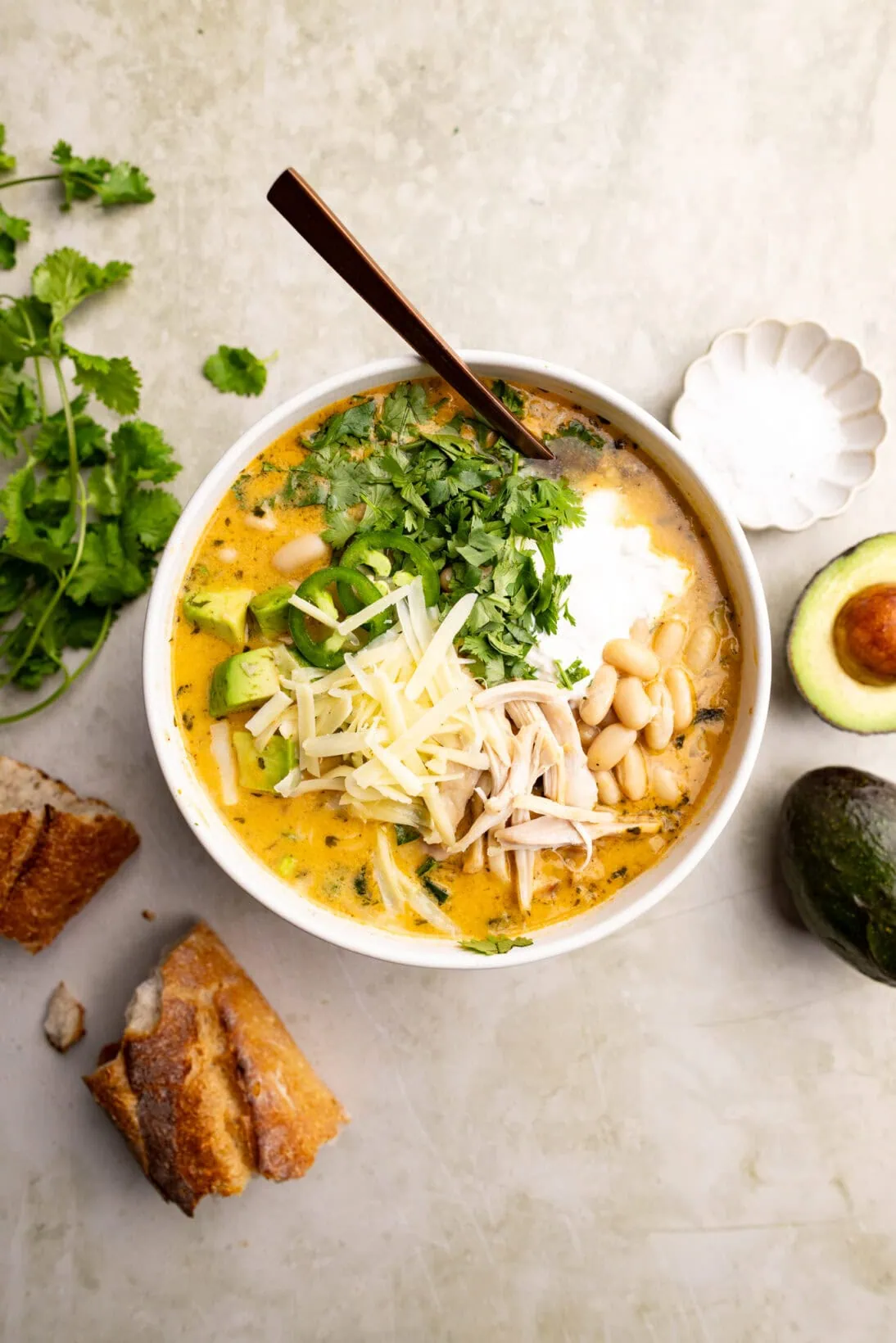 A bowl of white bean chicken chili topped with cheese, sour cream, and avocado. 
